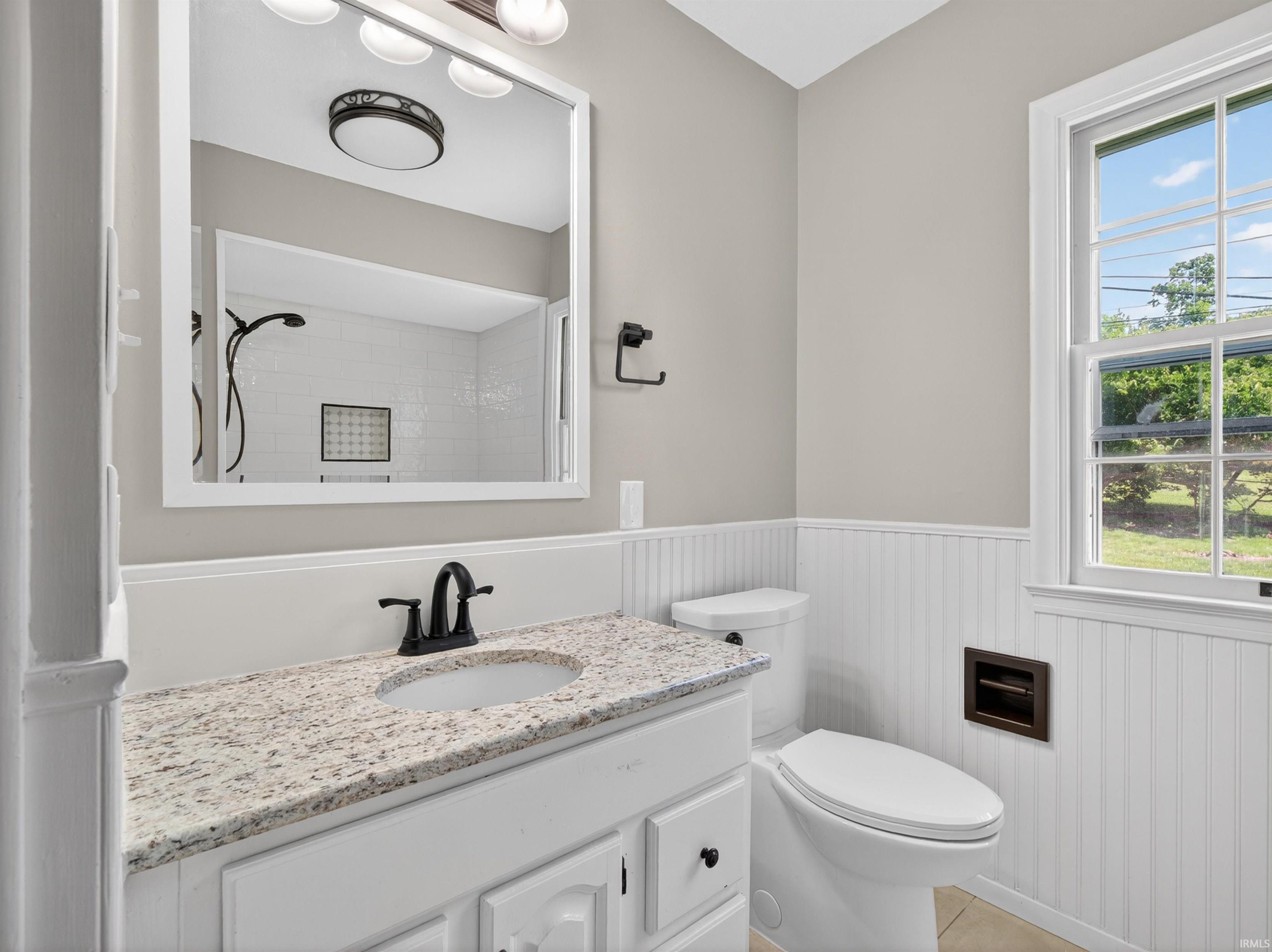 Bathroom featuring a white vanity with a speckled countertop, a toilet, and a window providing natural light