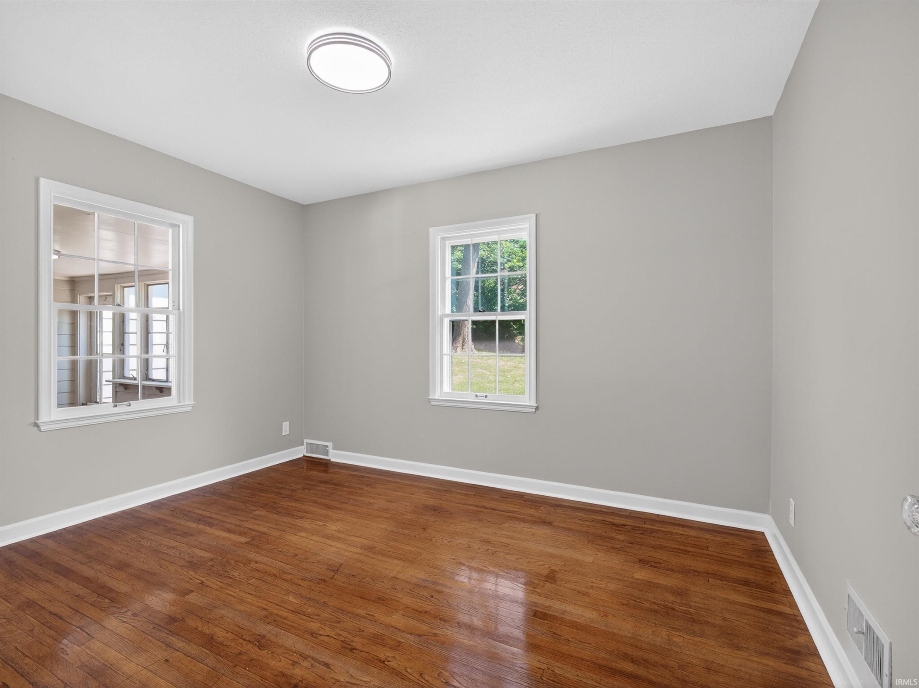Hardwood flooring complements light gray walls, white trim, and a contemporary ceiling light fixture