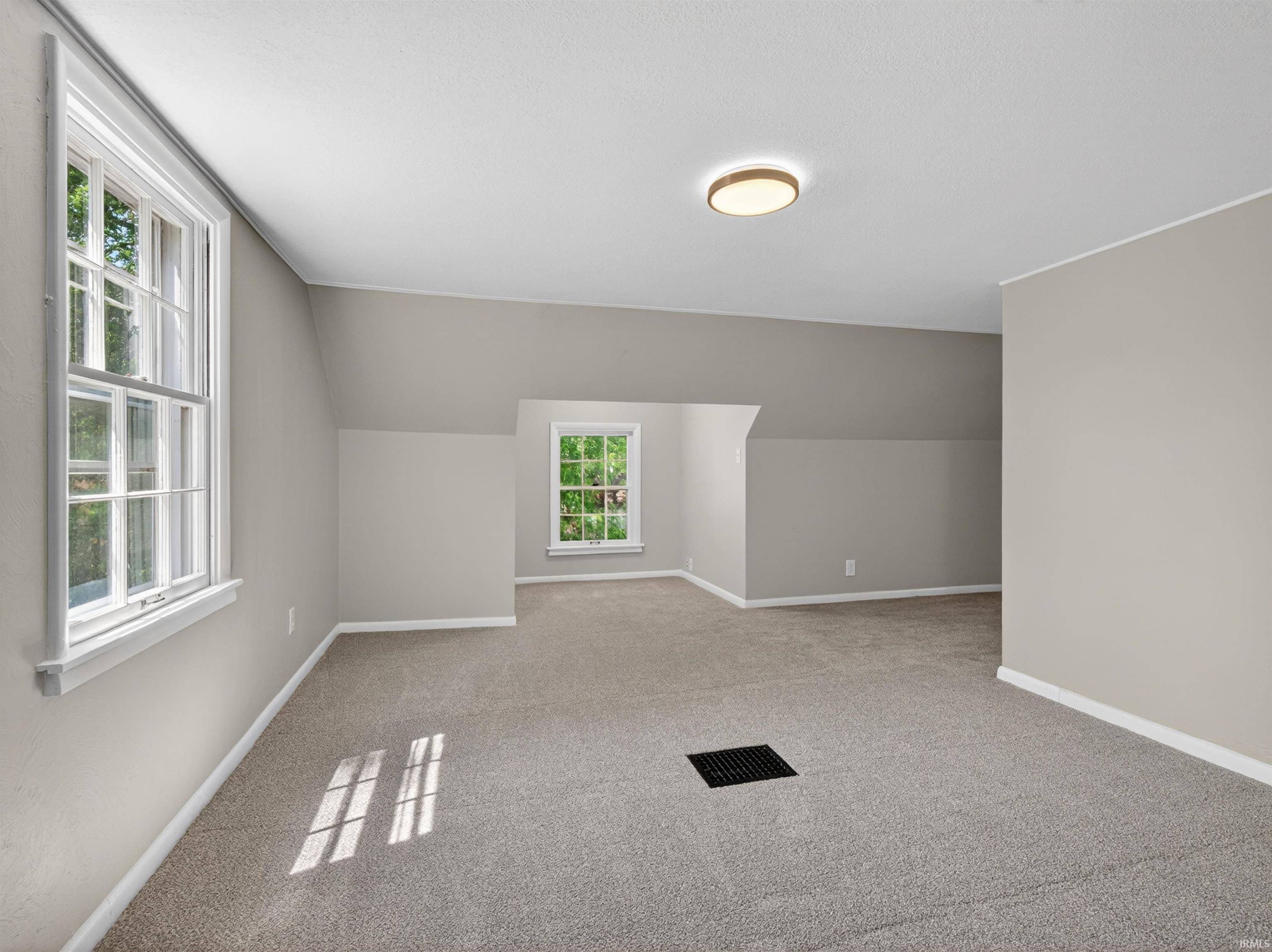 Spacious room featuring abundant natural light from multiple windows, neutral wall tones, low-pile carpeting, and a flush-mount ceiling light fixture