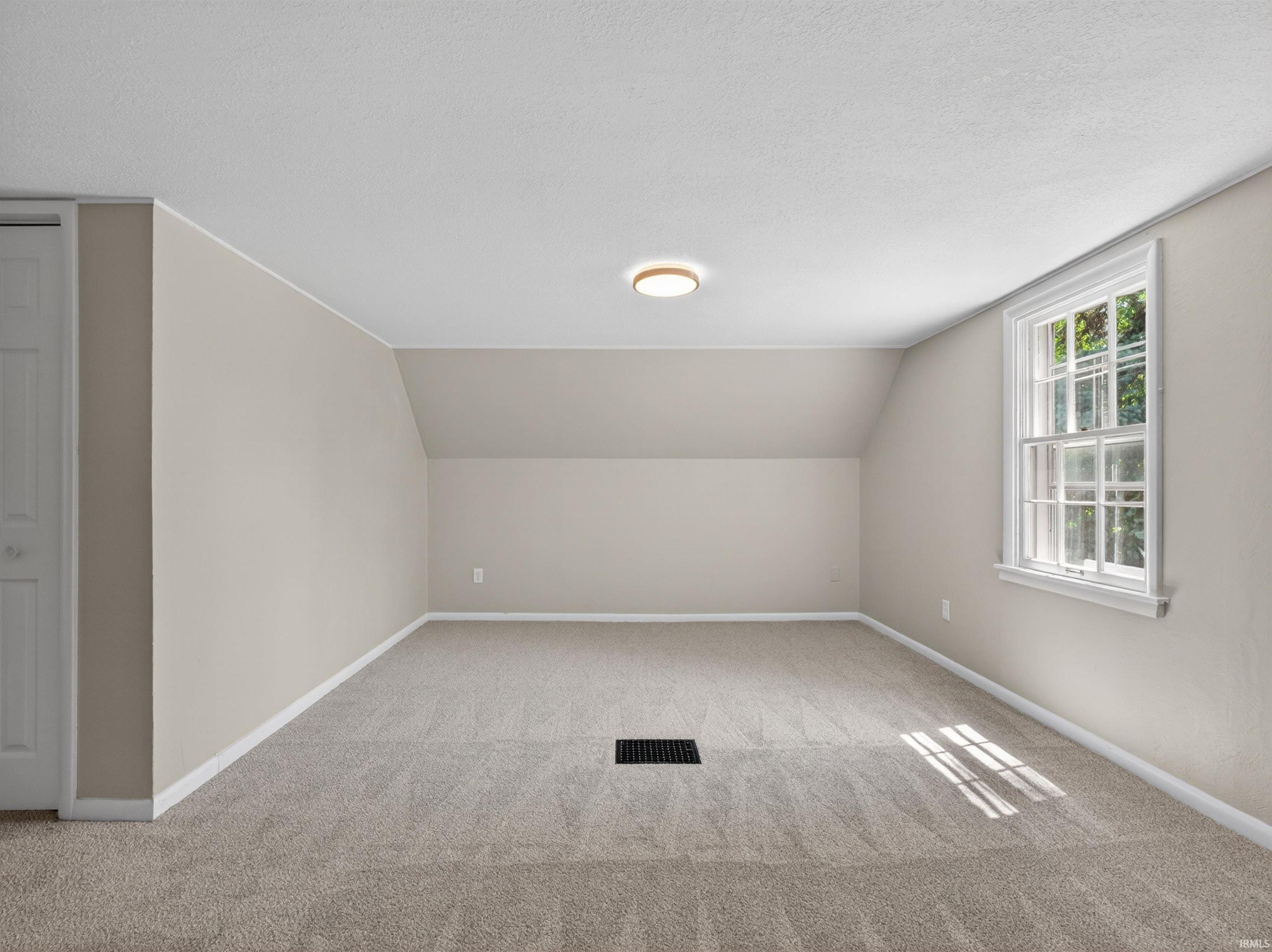 Carpeted room featuring a double-hung window, sloped ceilings, a flush mount ceiling light, and neutral wall paint