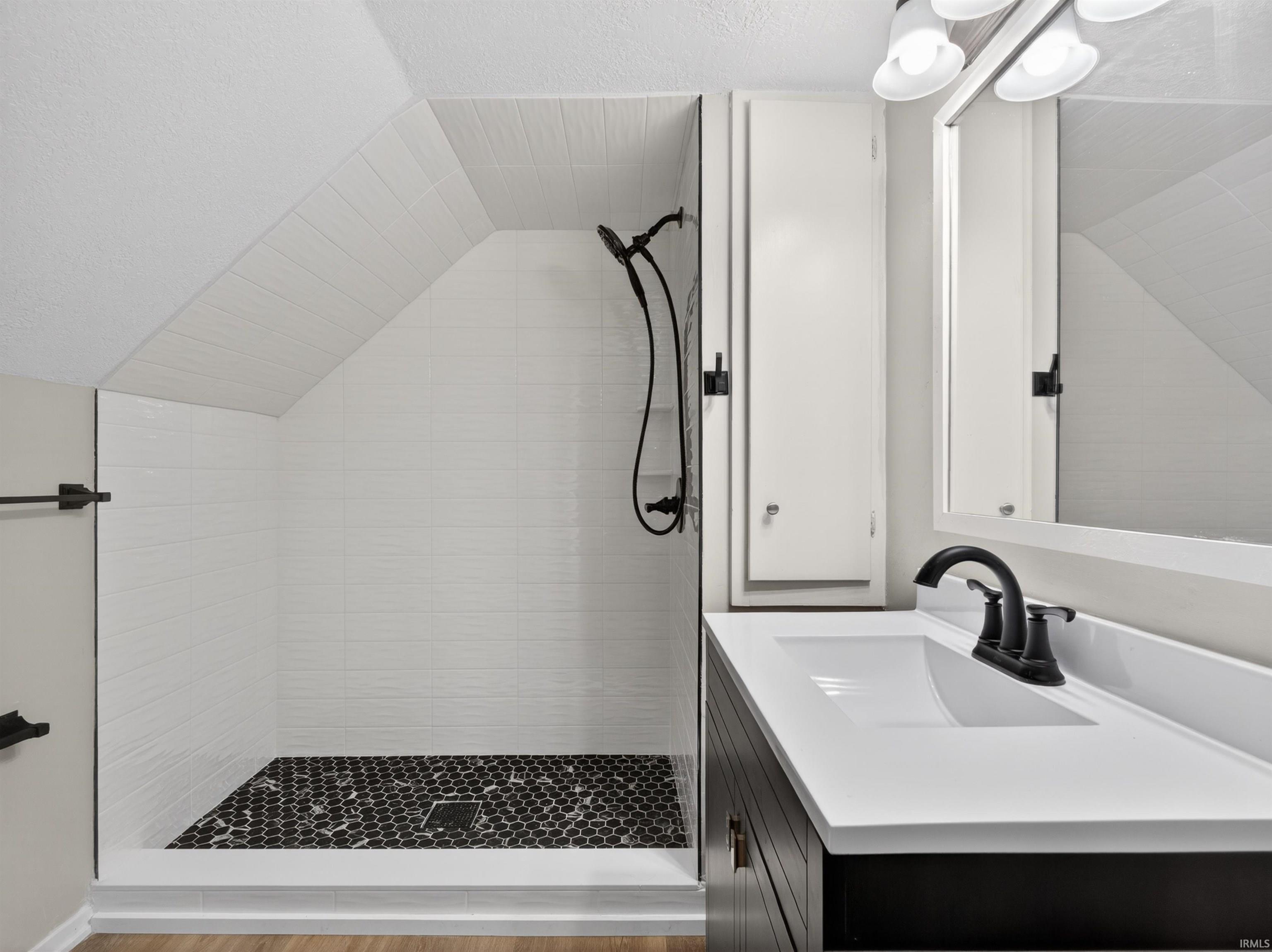 Modern bathroom featuring a walk-in shower with white subway tile walls and black hexagonal floor tiles