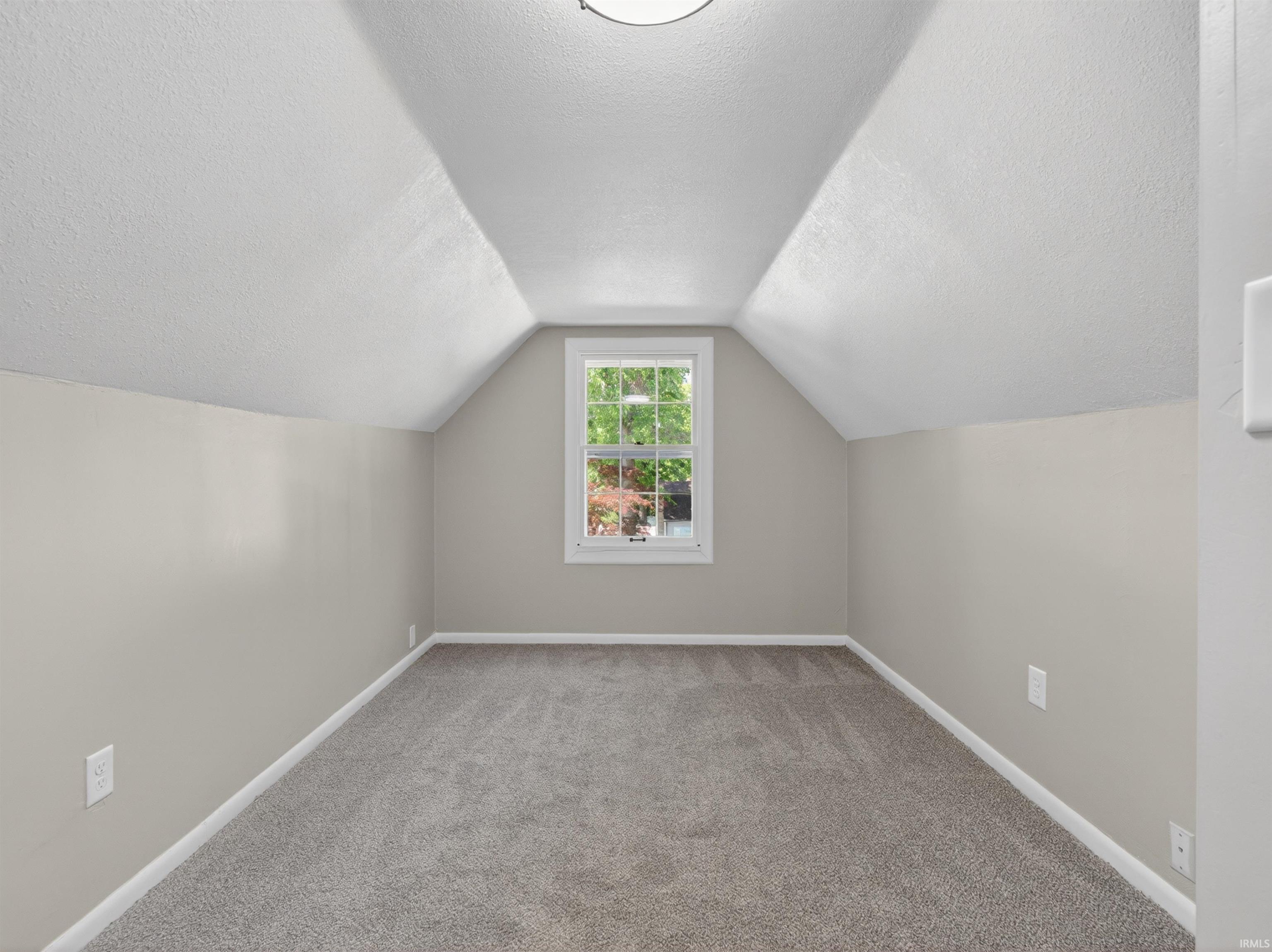 Recessed window with white trim, light gray painted walls, textured white sloped ceilings, and gray carpeted flooring