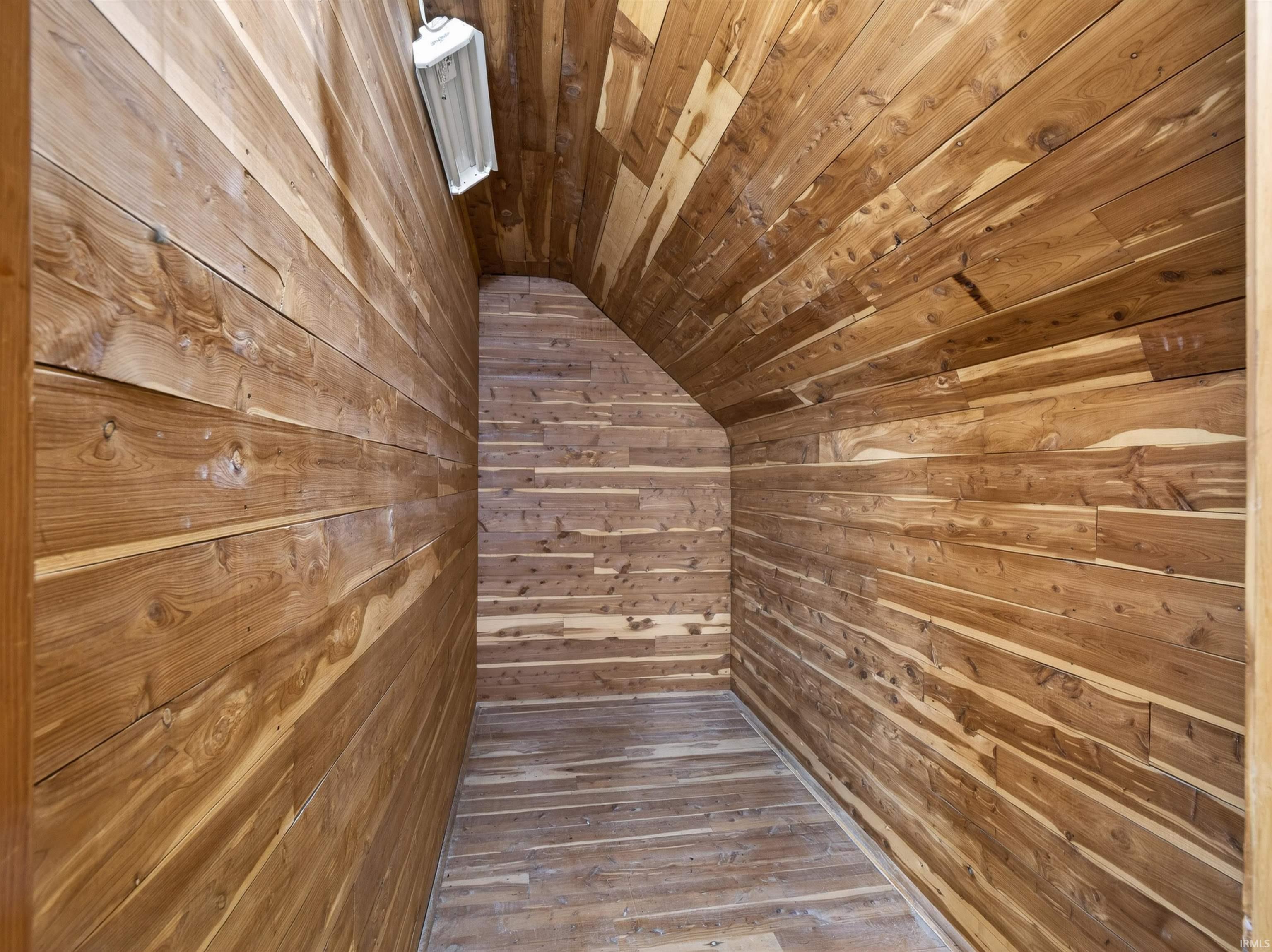 Storage area featuring wood paneling on walls and ceiling, wood-finish flooring, and sloped ceiling