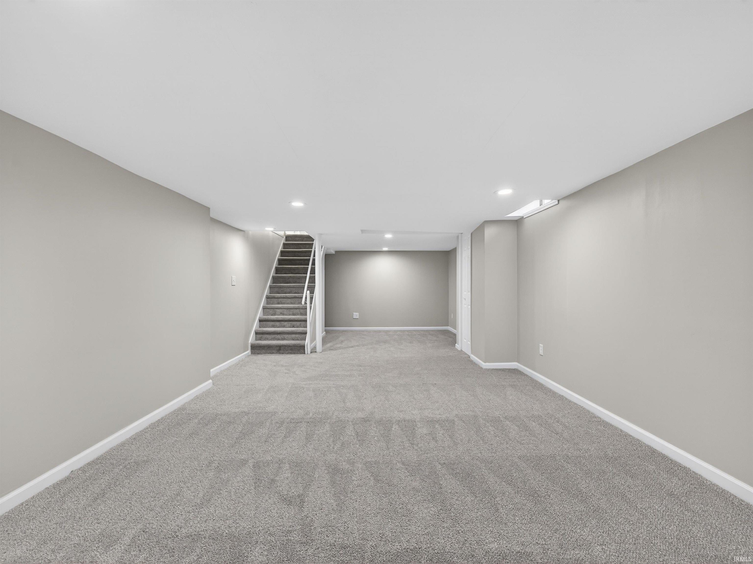 Spacious lower level featuring gray carpeting, light gray wall paint, recessed lighting, and a carpeted staircase with white railings