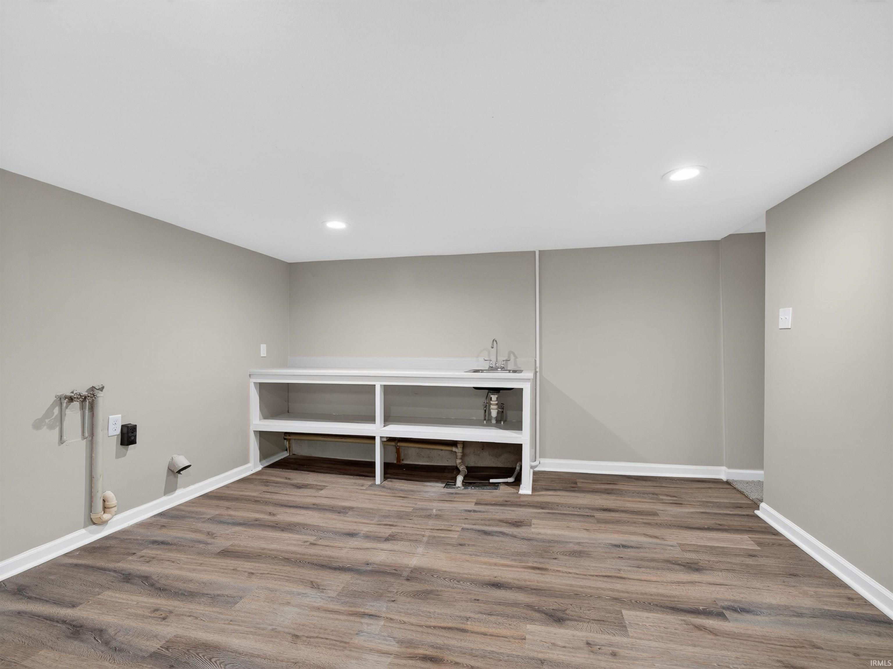 Spacious utility area featuring wood-finish flooring, light gray walls, recessed lighting, and a built-in utility sink with shelving