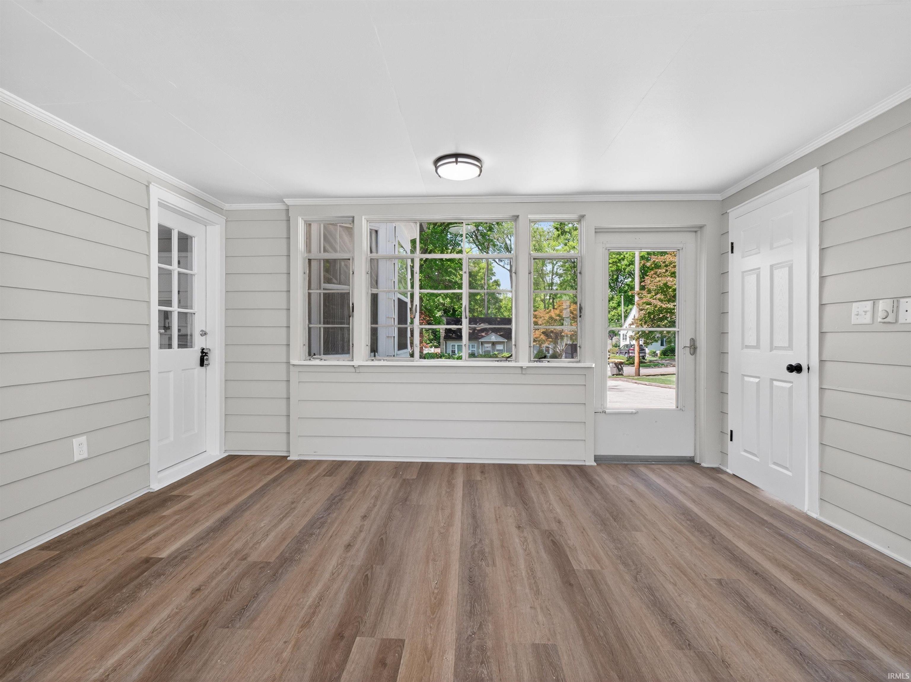 Spacious sunroom featuring wood-finish flooring and light gray horizontal plank walls