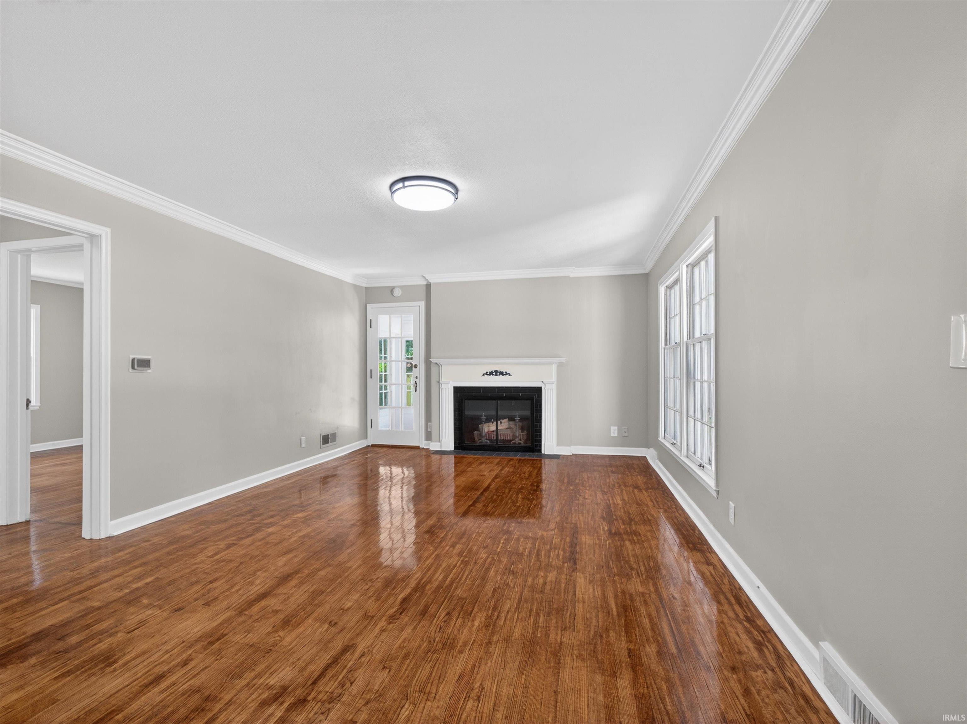 Spacious interior featuring wood-finish flooring, a white mantel fireplace, and crown molding