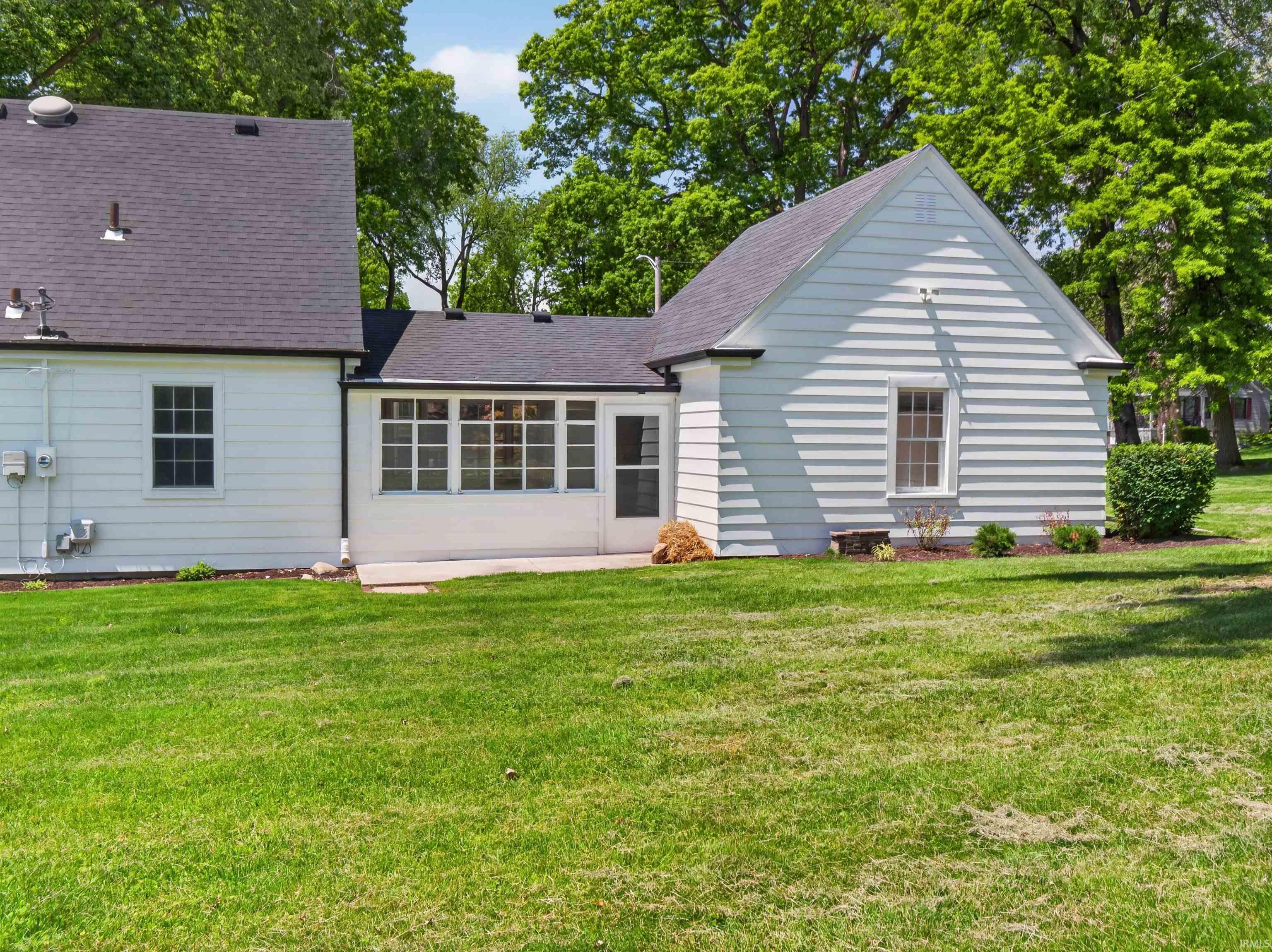 Expansive green lawn surrounds the white siding exterior with a dark shingle roof