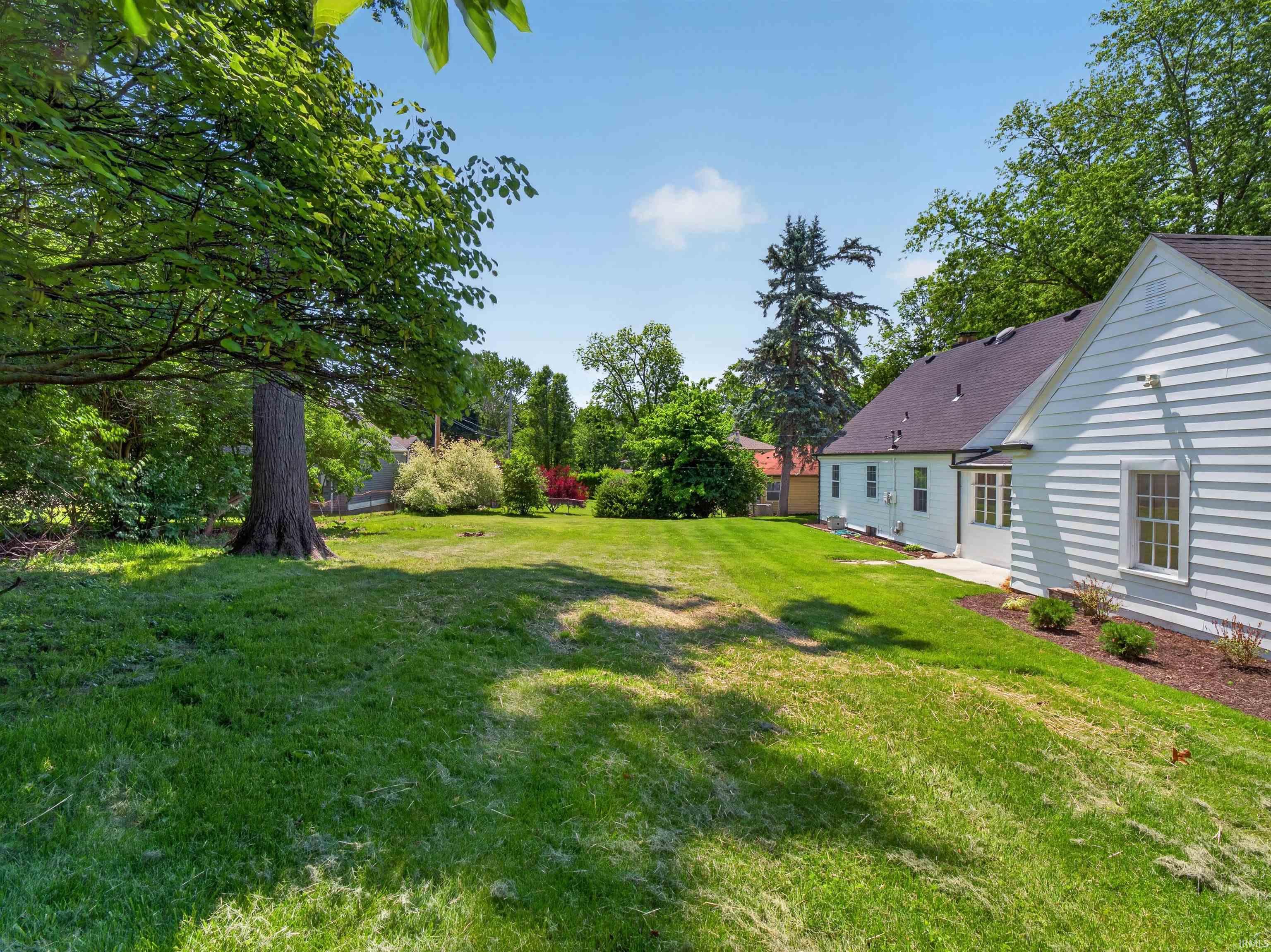 Expansive green lawn with mature trees and a traditional white siding exterior