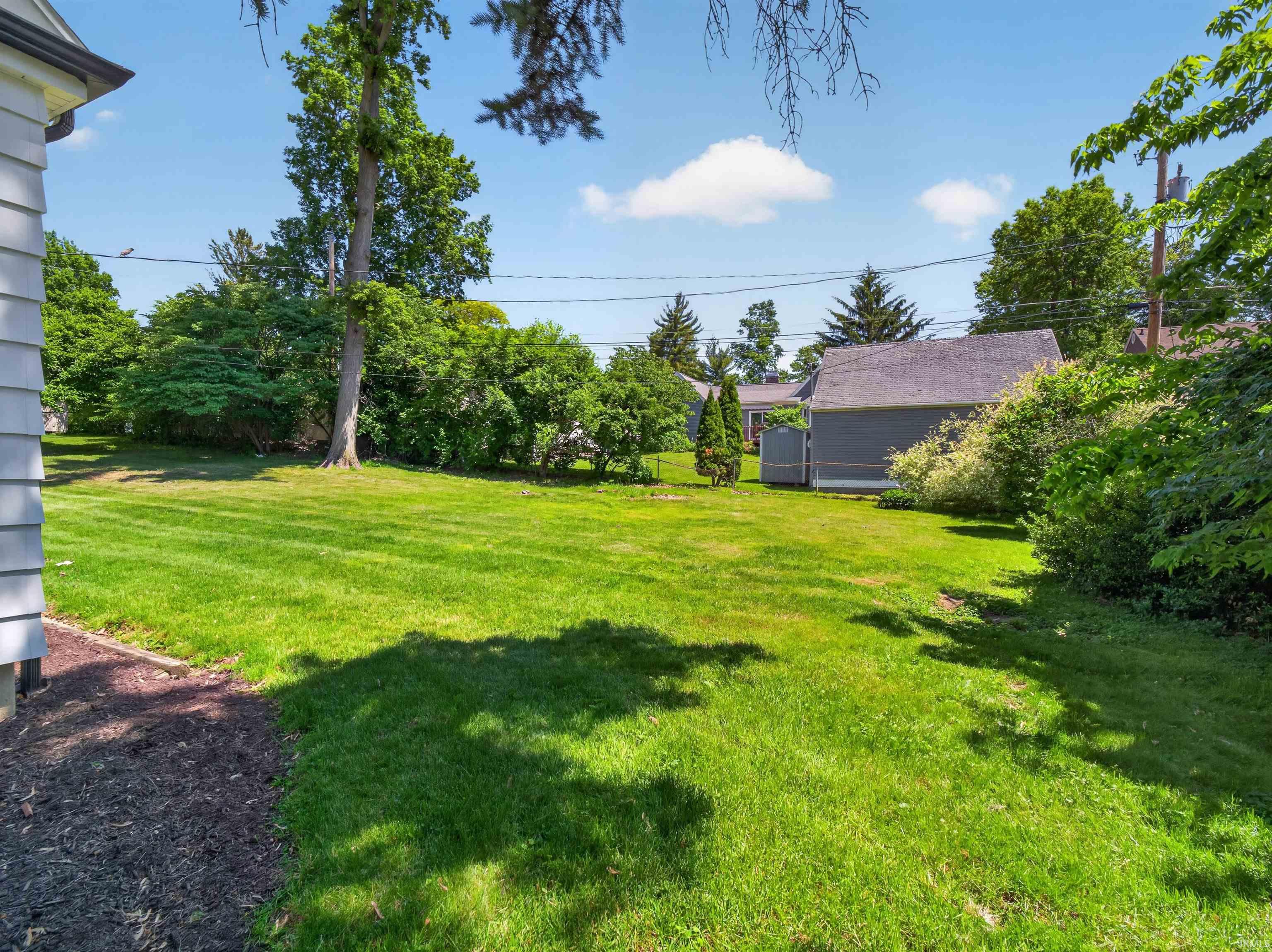 Expansive green lawn with mature trees and established perimeter shrubbery