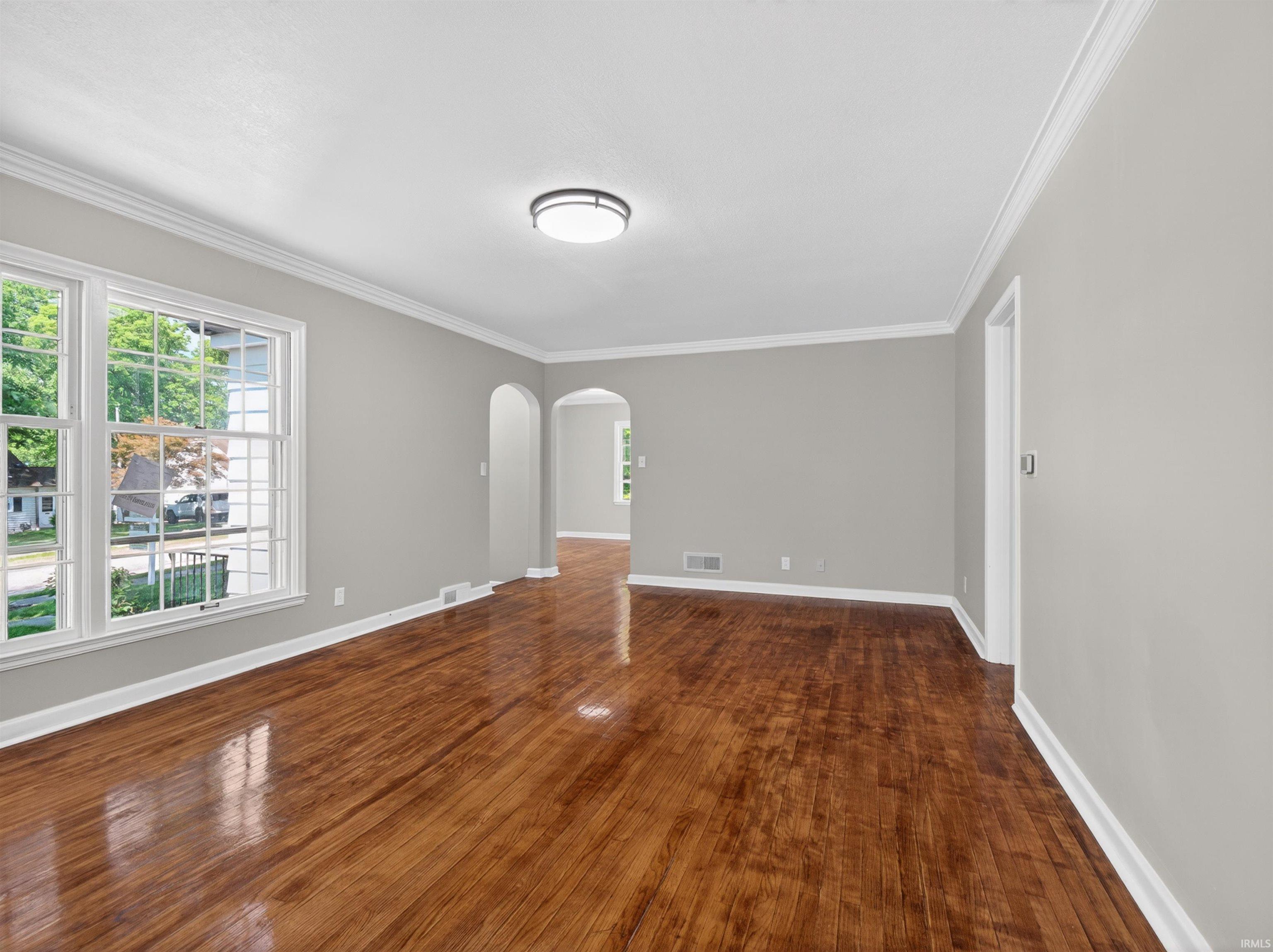 Spacious living area featuring polished wood-finish flooring, light gray wall paint, and white trim