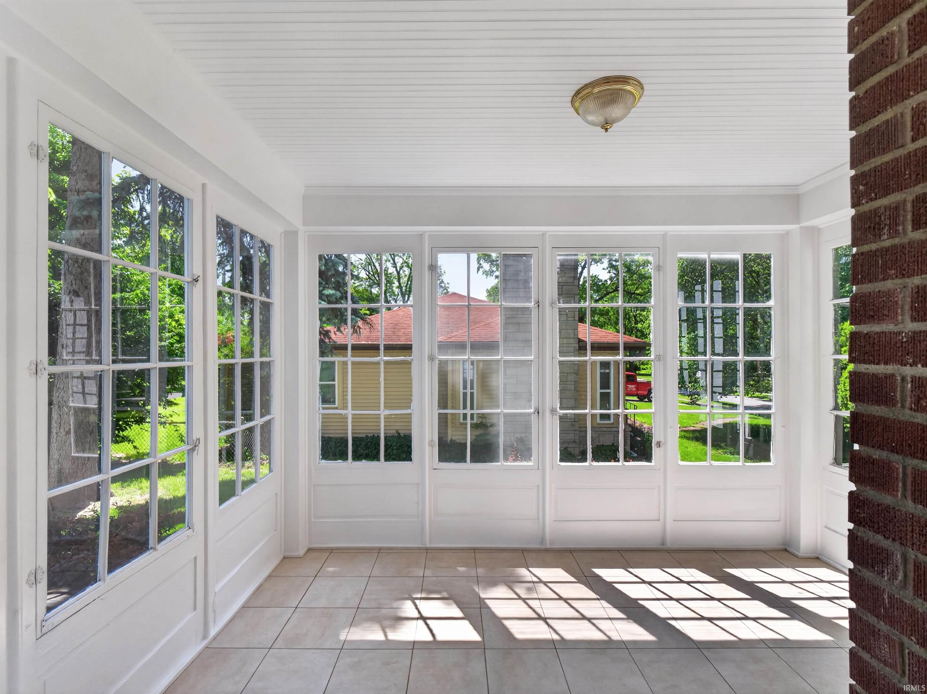 Sunroom featuring large paneled windows, tiled flooring, a beadboard ceiling, and an exposed brick column