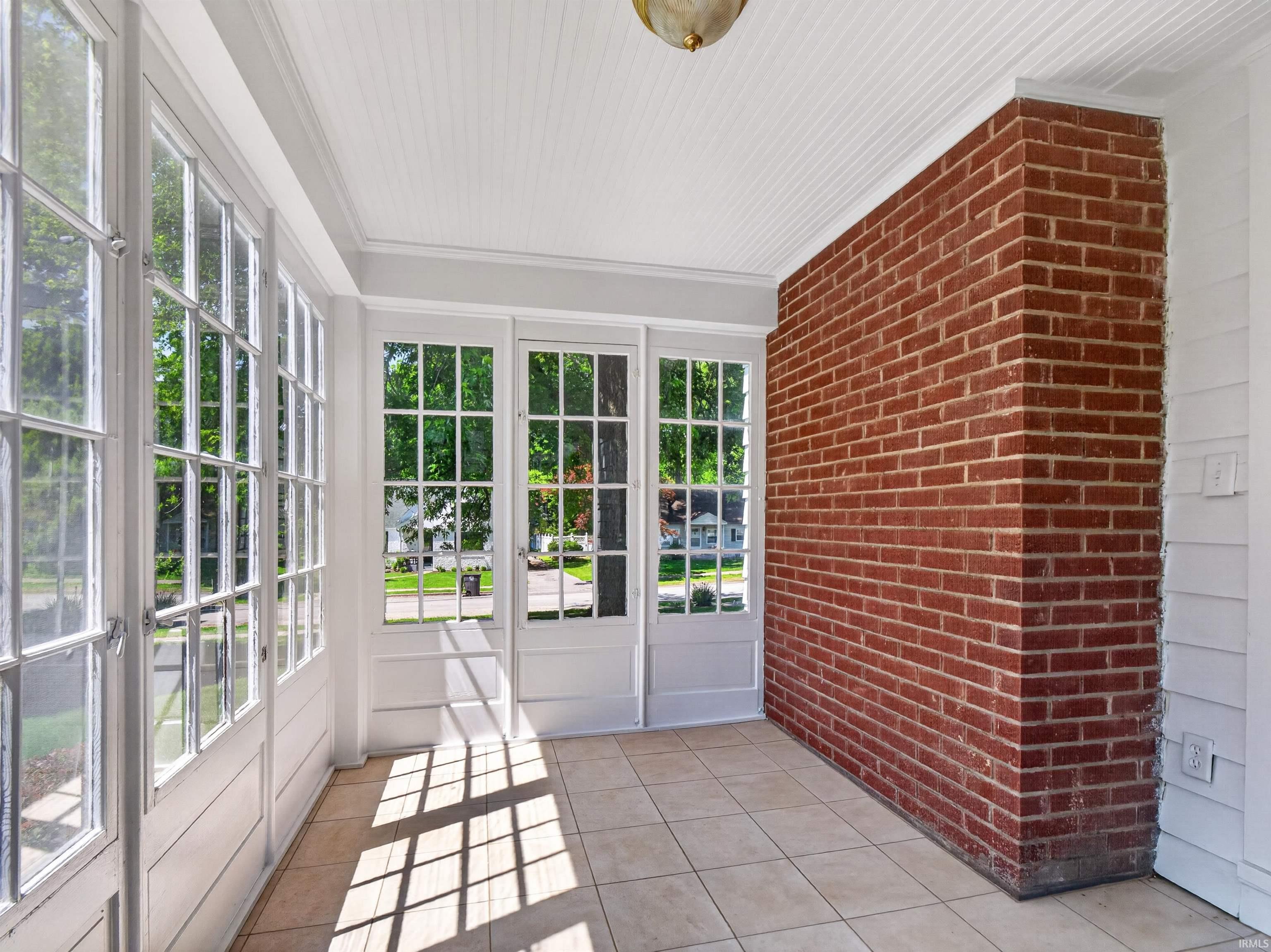 Sunroom featuring extensive grid-pattern windows, a red brick accent wall, tiled flooring, white beadboard ceiling, and white painted shiplap paneling