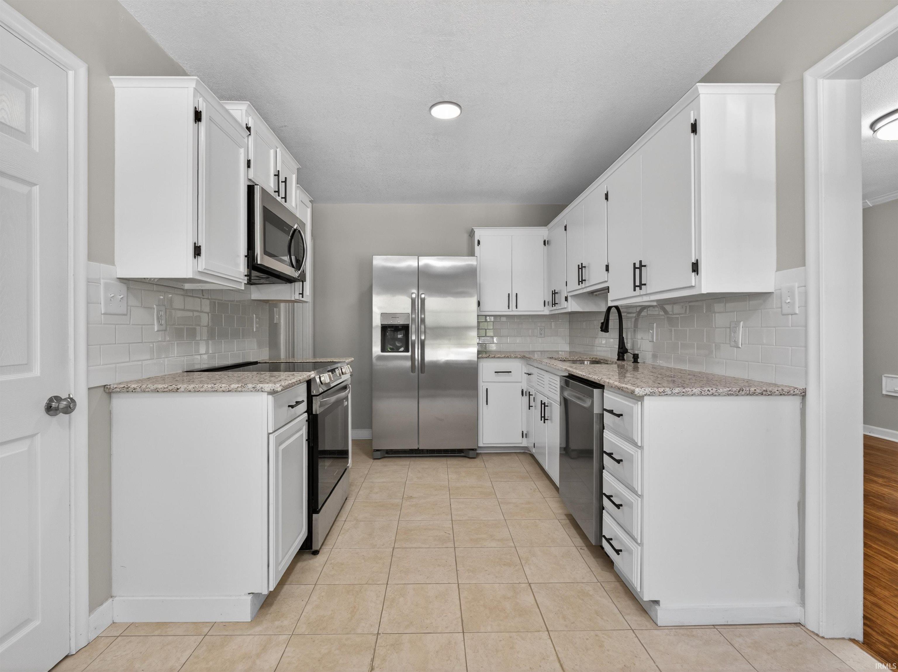 U-shaped kitchen featuring white cabinetry, light-colored countertops, stainless steel appliances, a white subway tile backsplash, and light-colored tile flooring