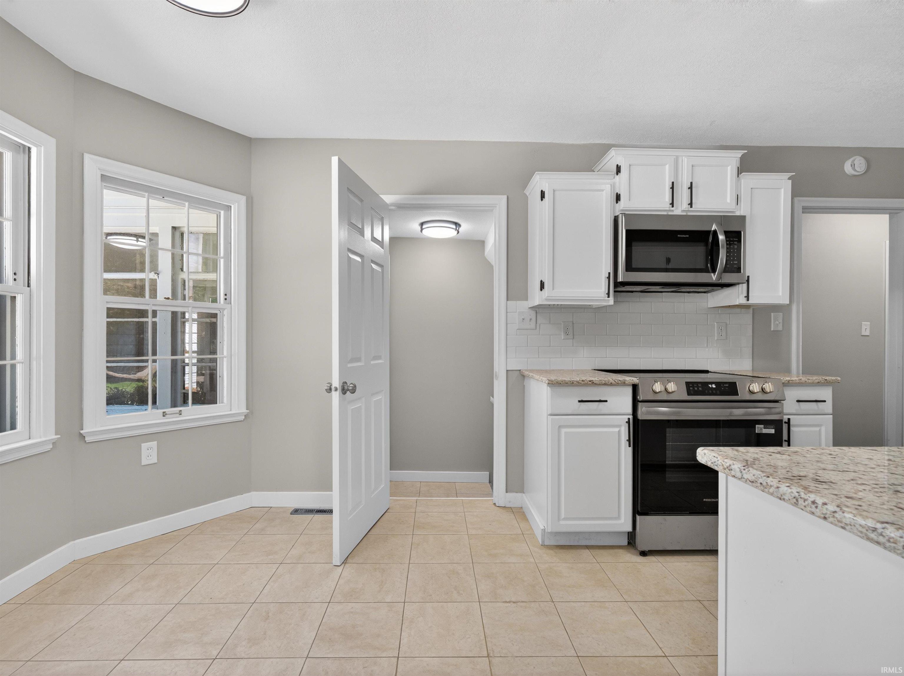 Kitchen area featuring white cabinetry, stainless steel appliances, a tile backsplash, and light-toned tile flooring