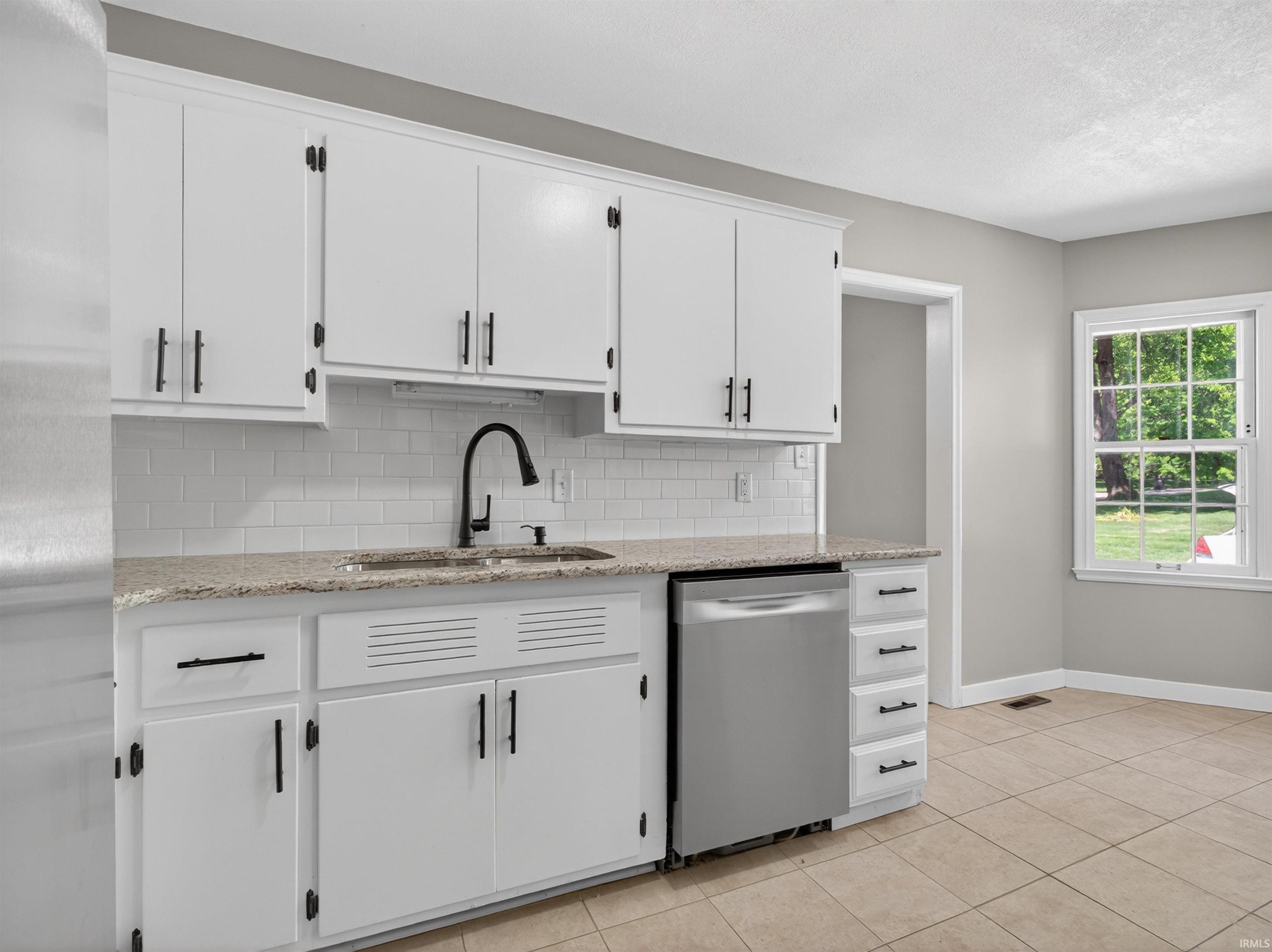 Kitchen featuring white cabinetry with black hardware, a stainless steel dishwasher, a black gooseneck faucet, light granite-finish countertops, and a white subway tile backsplash
