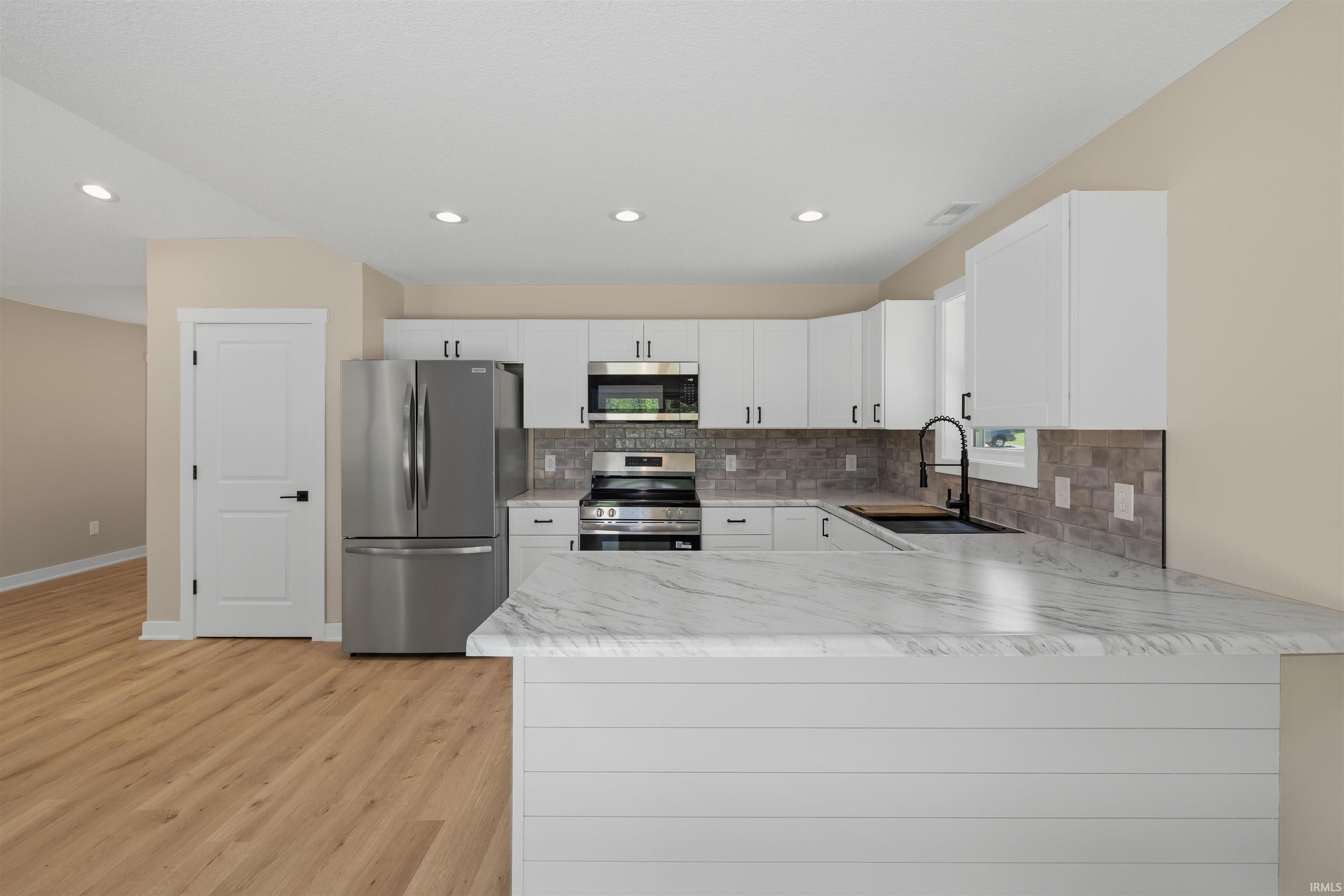 Kitchen featuring white shaker cabinetry with black hardware, stainless steel appliances, and a mosaic tile backsplash