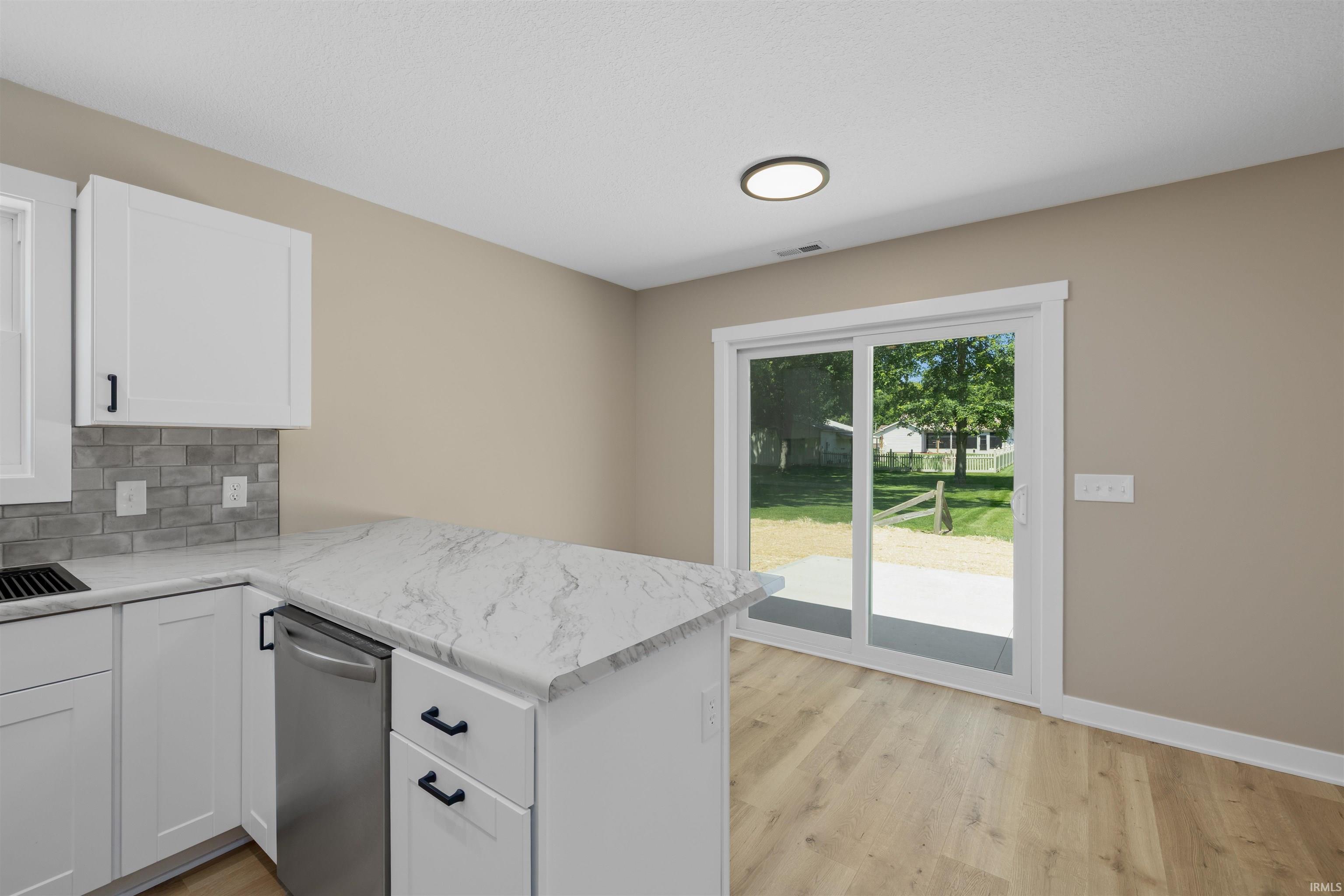 Kitchen featuring a white shaker cabinetry, patterned stone-finish countertops, stainless steel dishwasher, and a gray subway tile backsplash