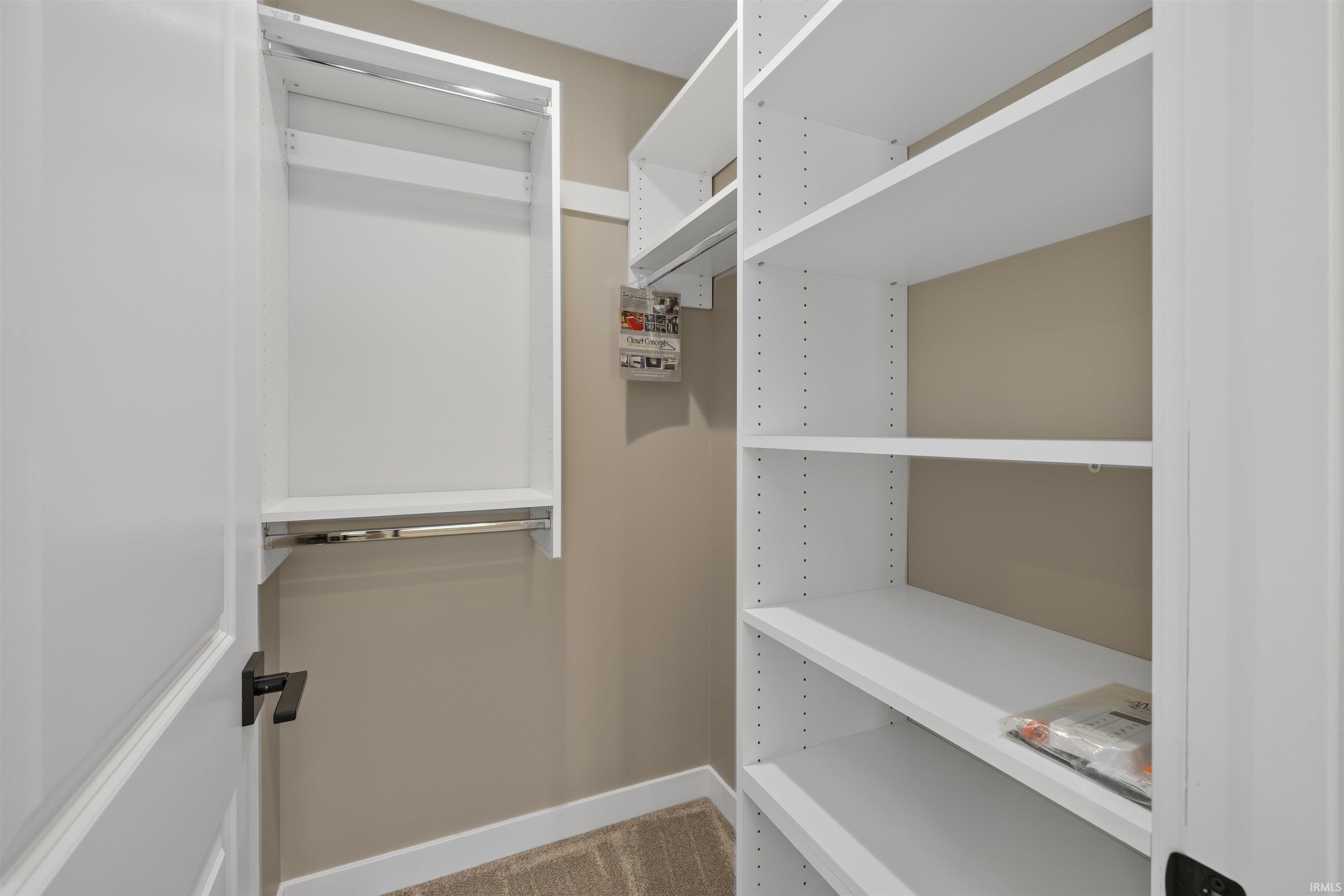 Walk-in closet featuring white built-in shelving, two hanging rods, and a neutral wall color