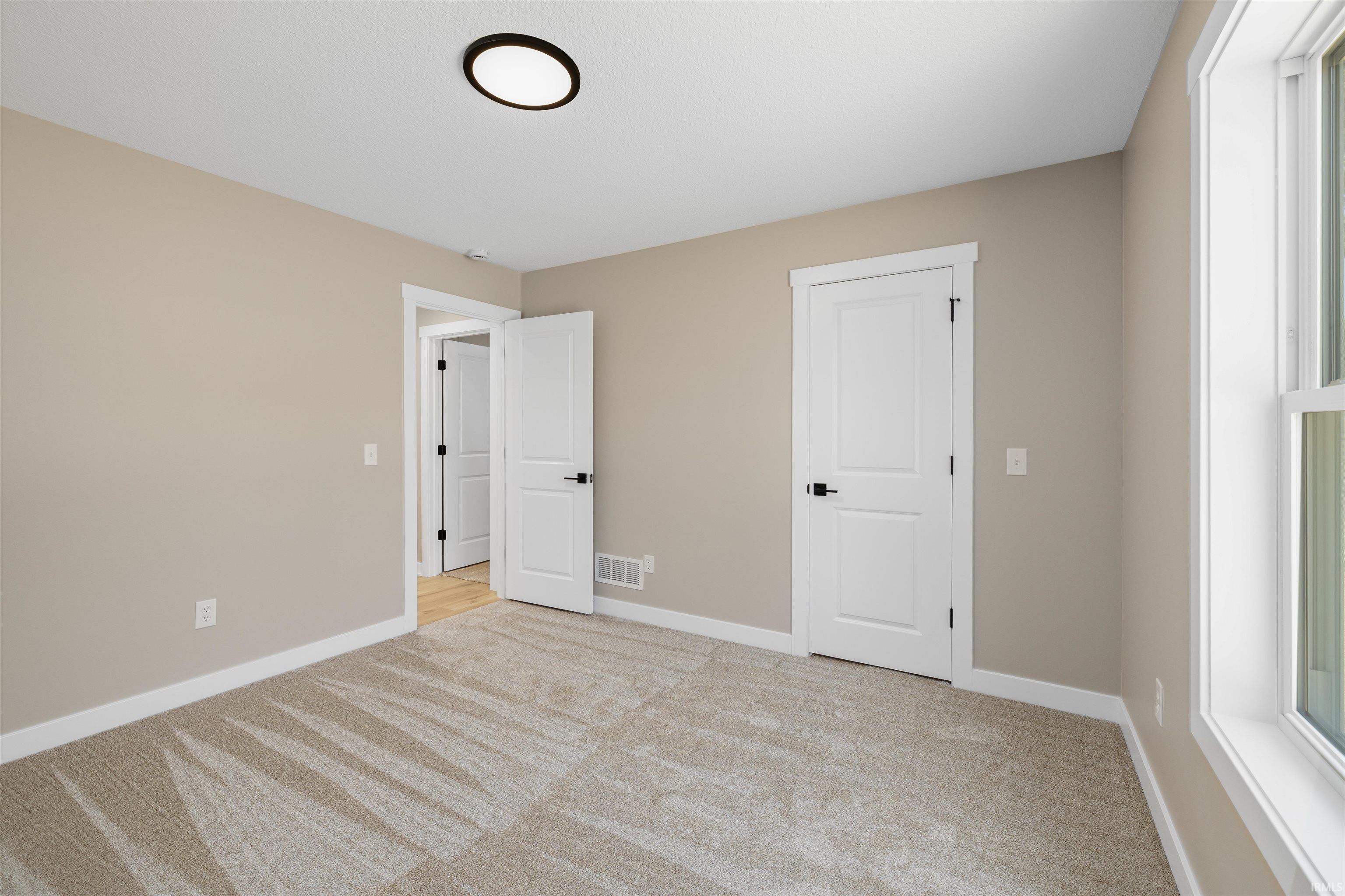 Carpeted room featuring neutral-toned walls, white trim, and a contemporary flush-mount ceiling light