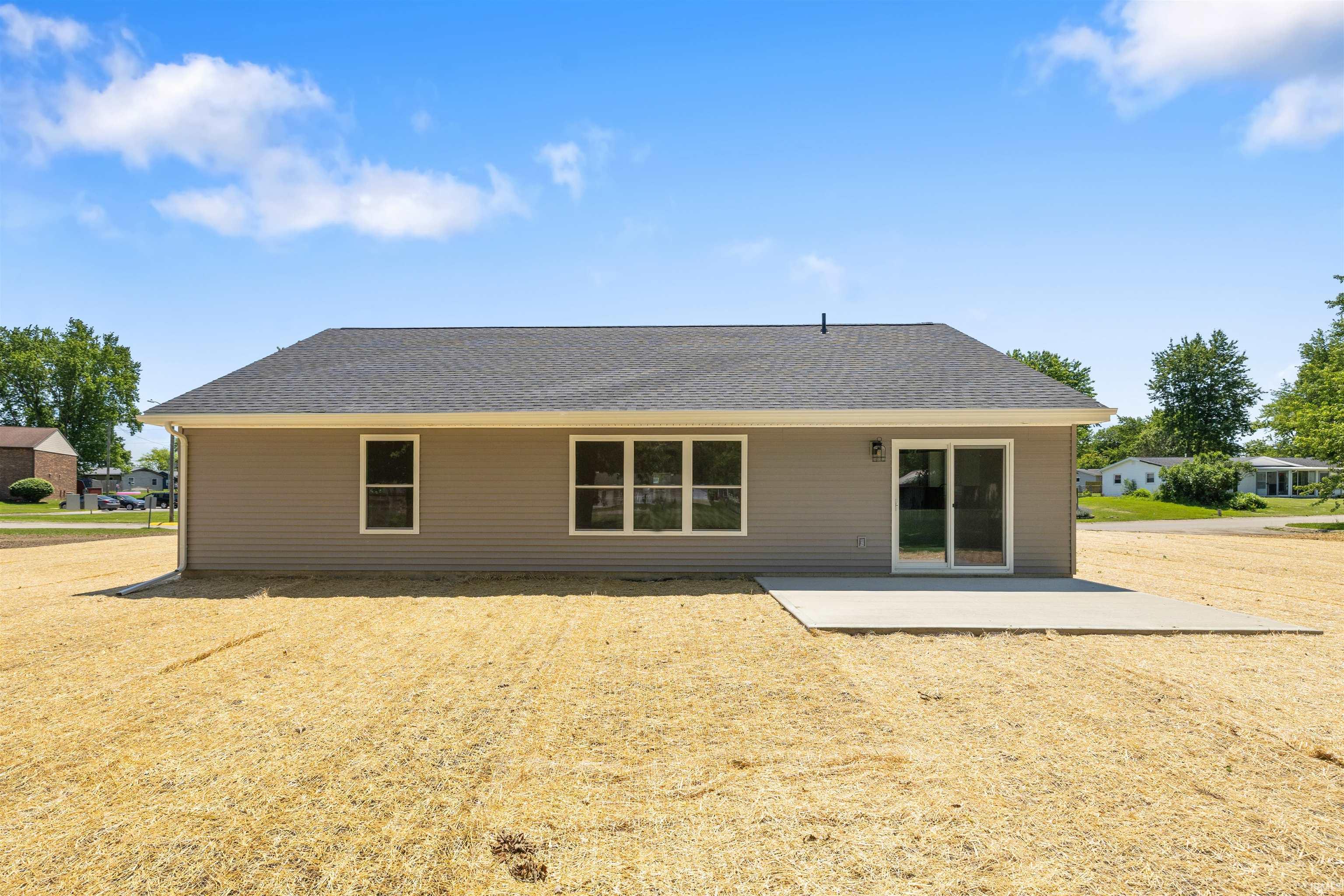 Rear exterior featuring tan horizontal siding, a dark shingle roof, multiple windows, and a sliding glass door