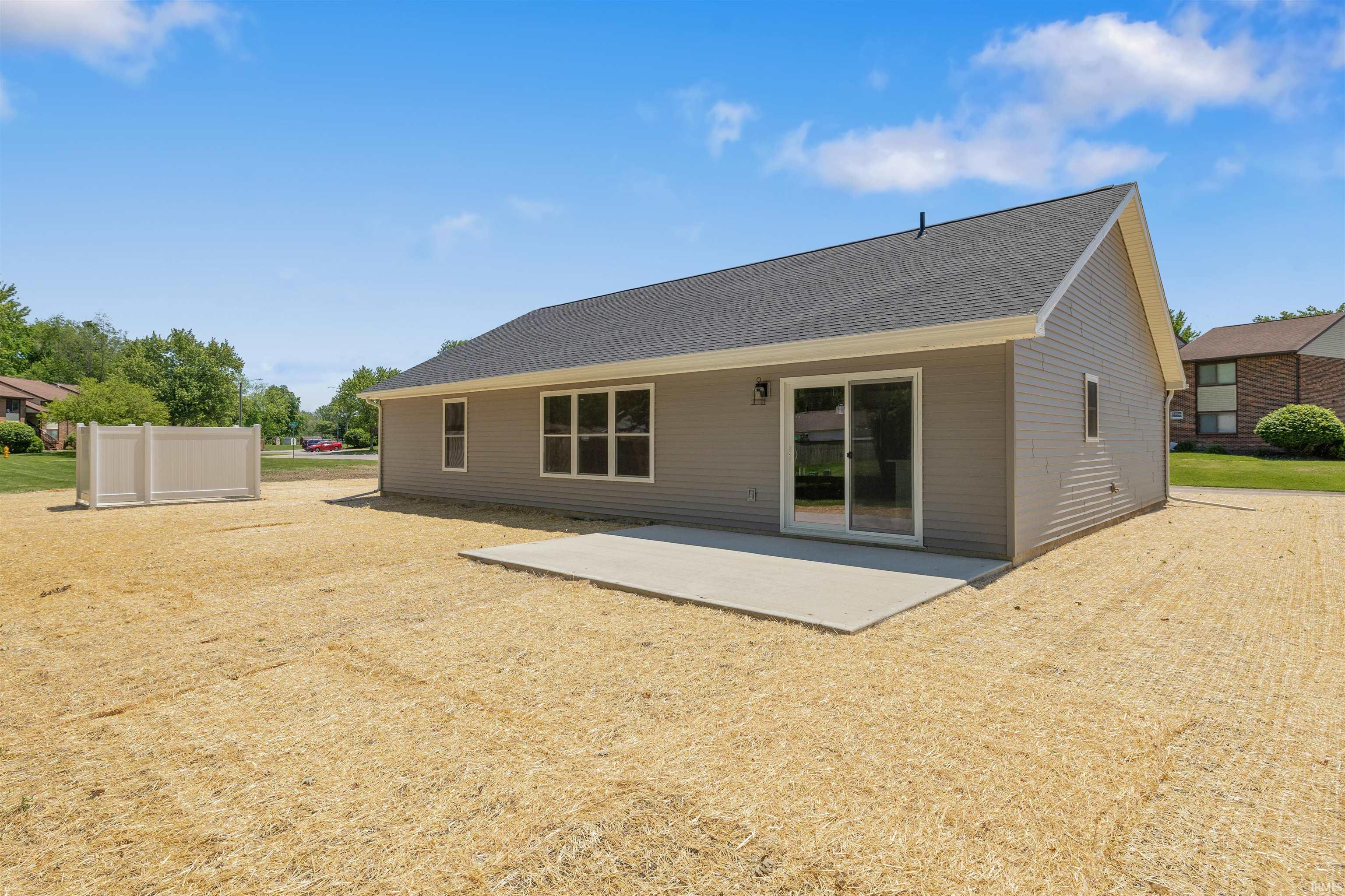 Rear exterior featuring gray siding, a dark shingle roof, and a concrete patio