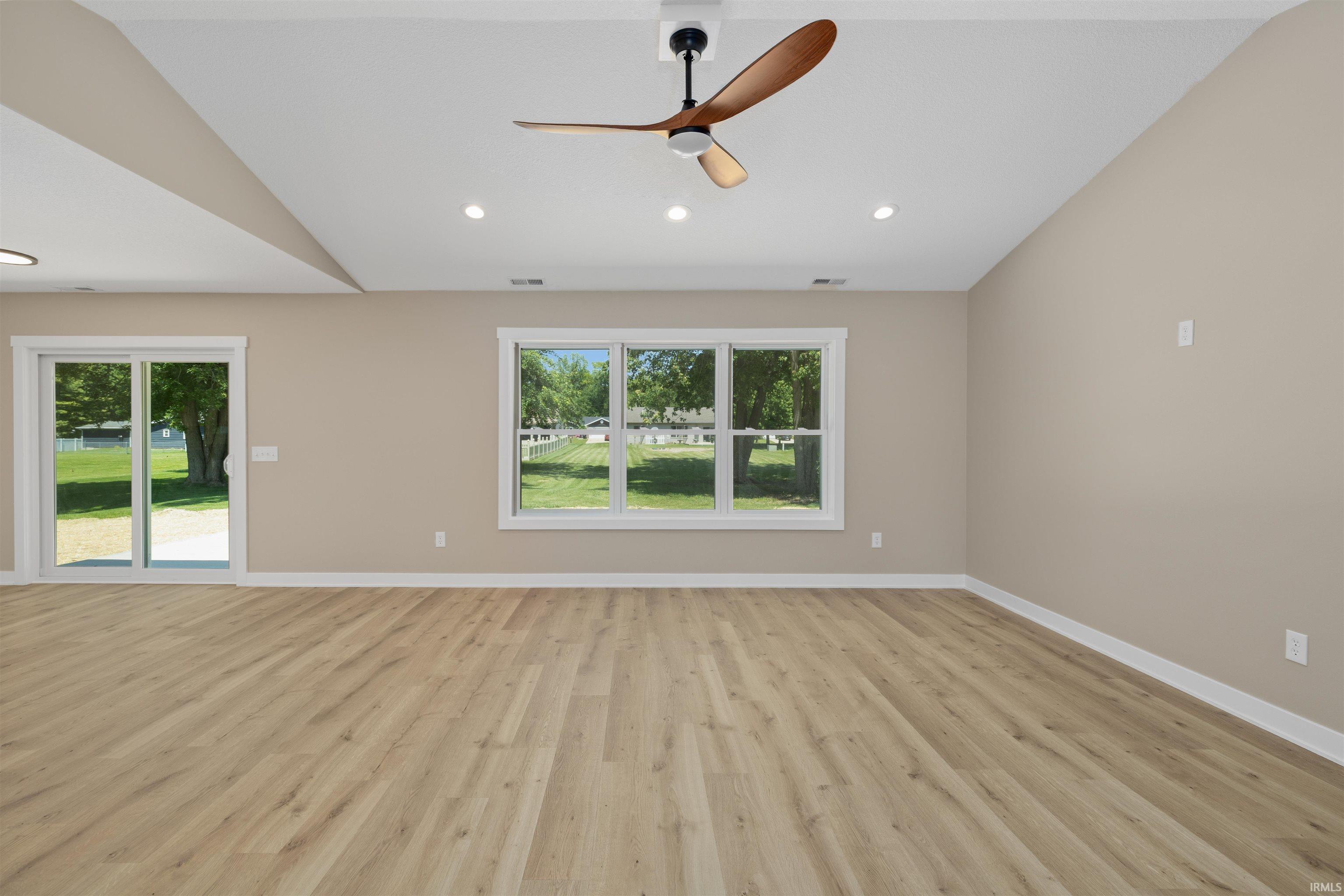 Spacious room featuring wood-finish flooring, a vaulted ceiling, and recessed lighting
