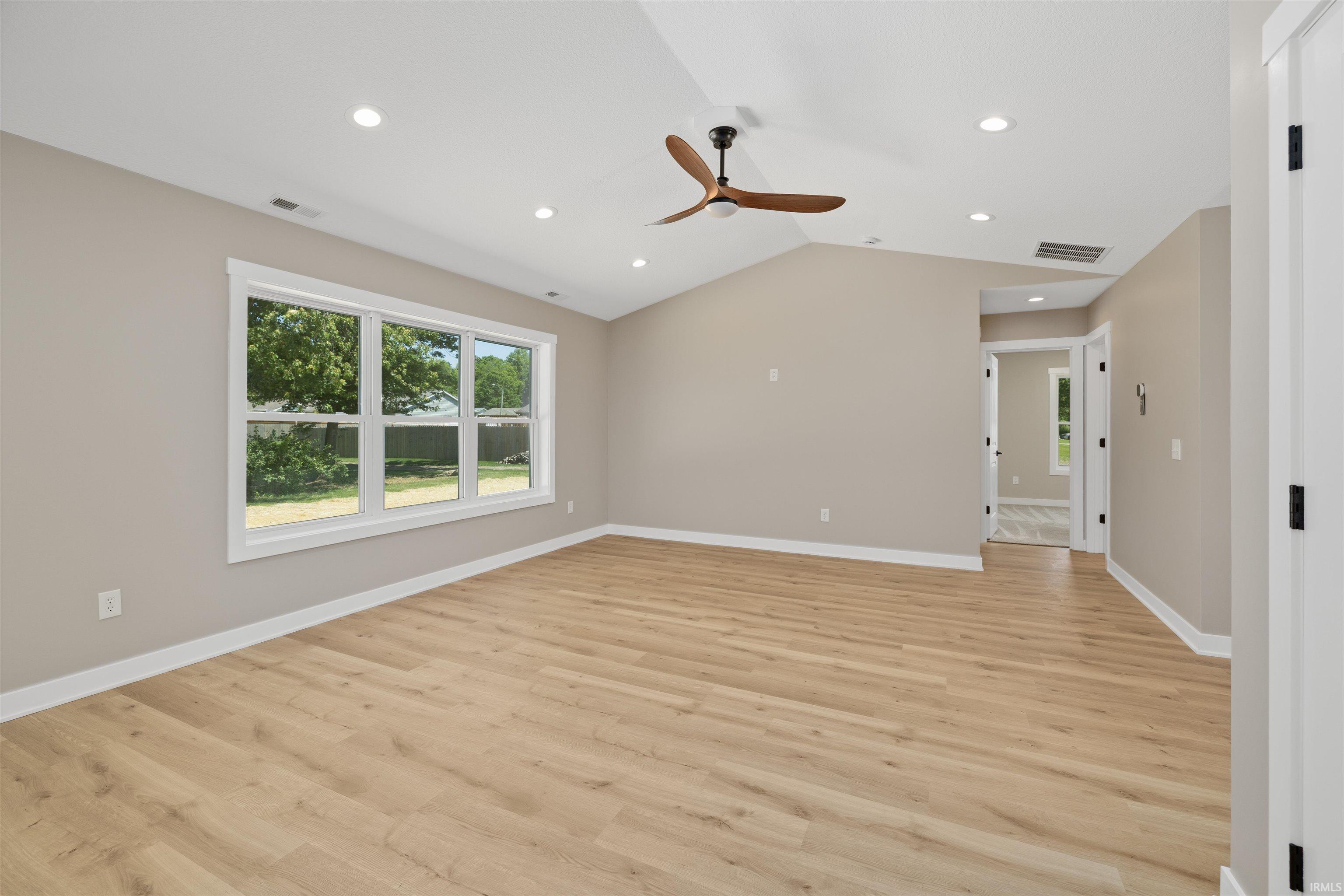 Spacious room featuring vaulted ceilings, recessed lighting, wood-finish flooring, a contemporary ceiling fan, and multiple windows with white trim