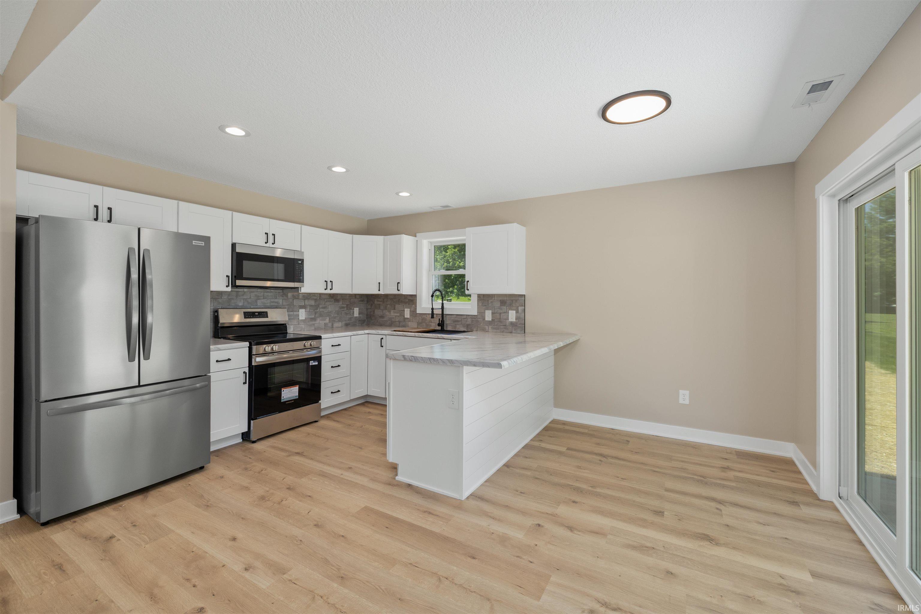 Modern kitchen featuring white cabinetry, stainless steel appliances, light wood-finish flooring, and a sliding glass door to the exterior