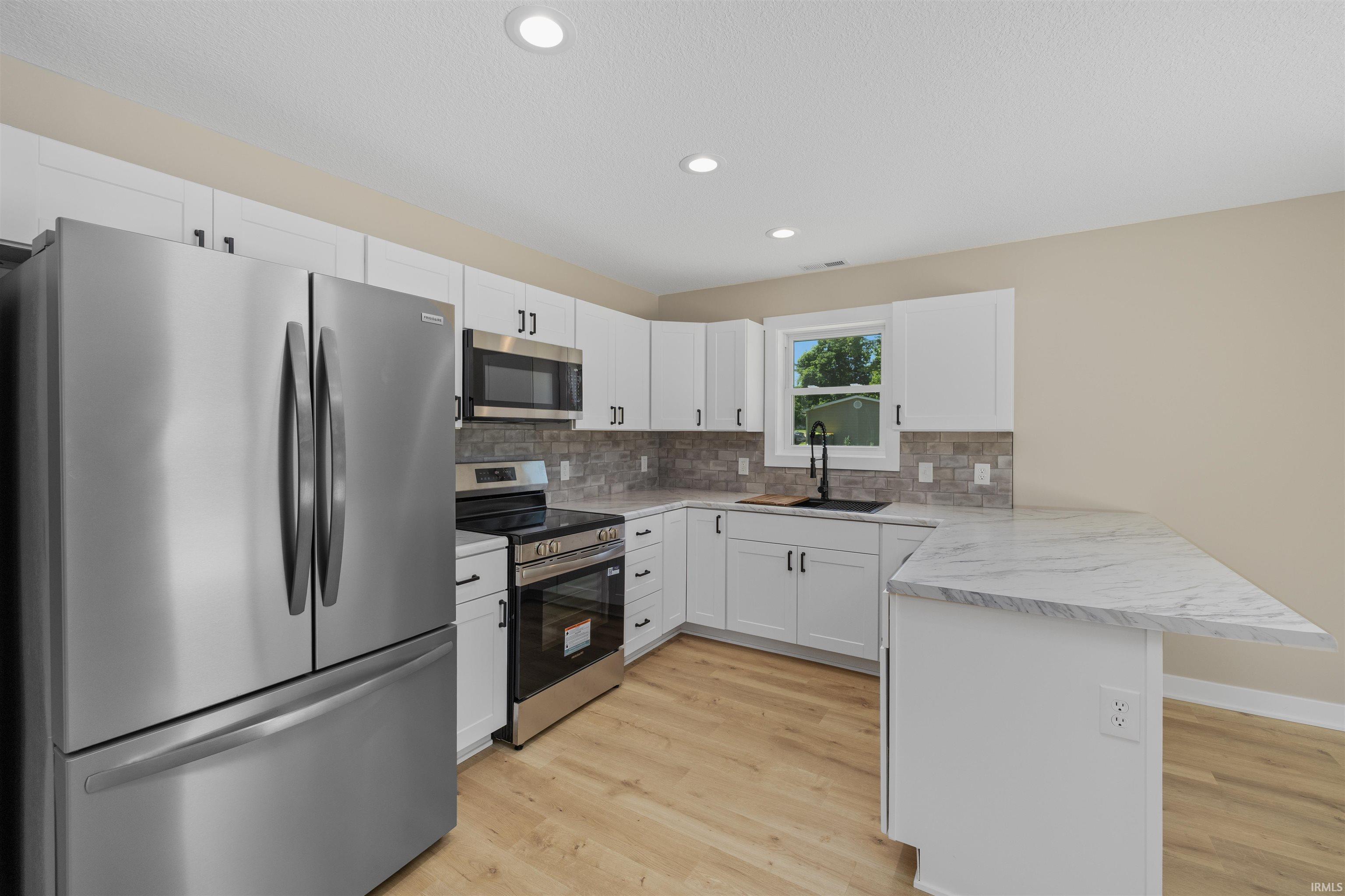 Kitchen featuring white cabinetry, stainless steel appliances, a white marble-look countertop, light wood-finish flooring, and recessed lighting