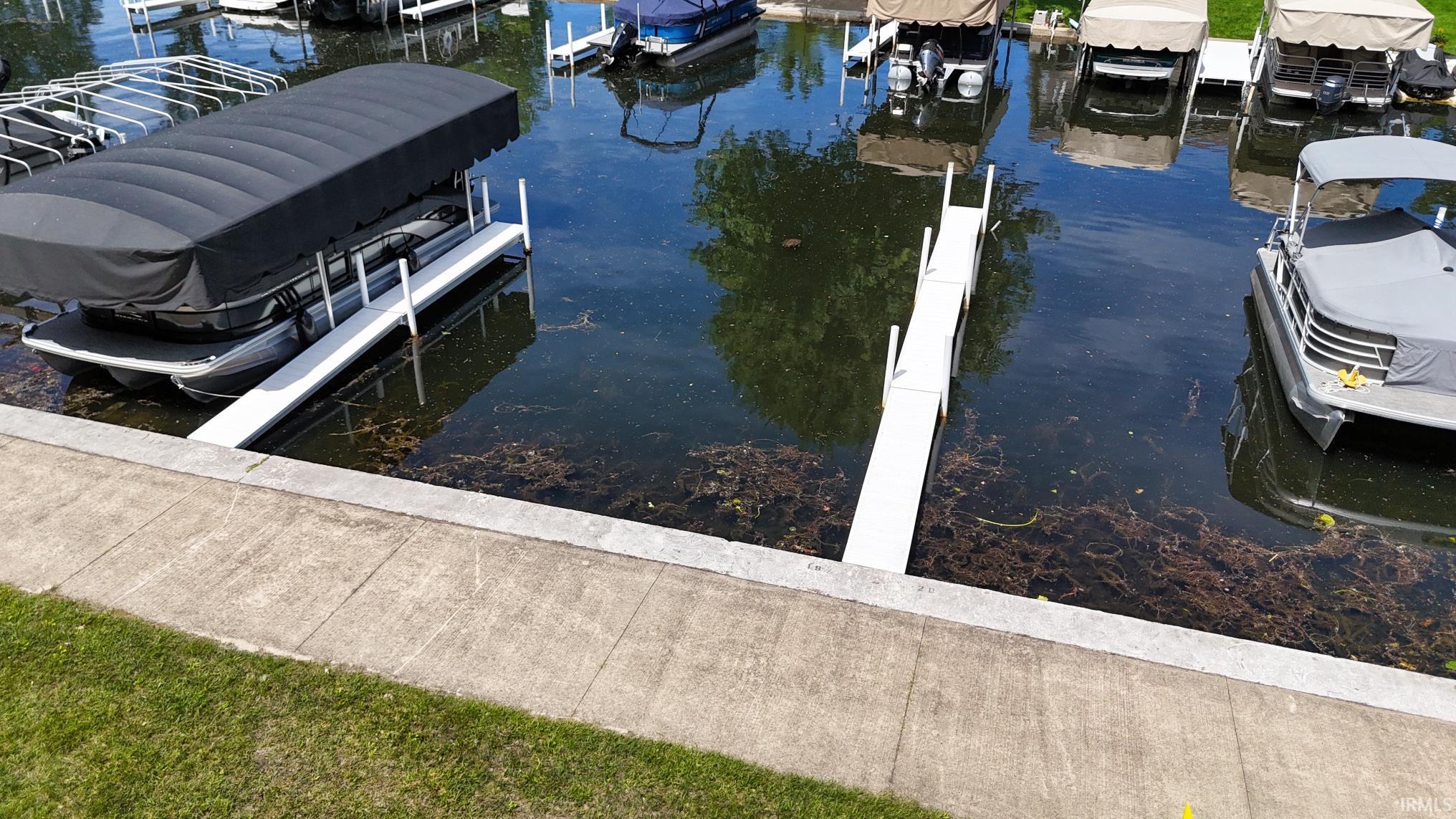 Waterfront property with multiple boat slips, concrete retaining wall, and green lawn space