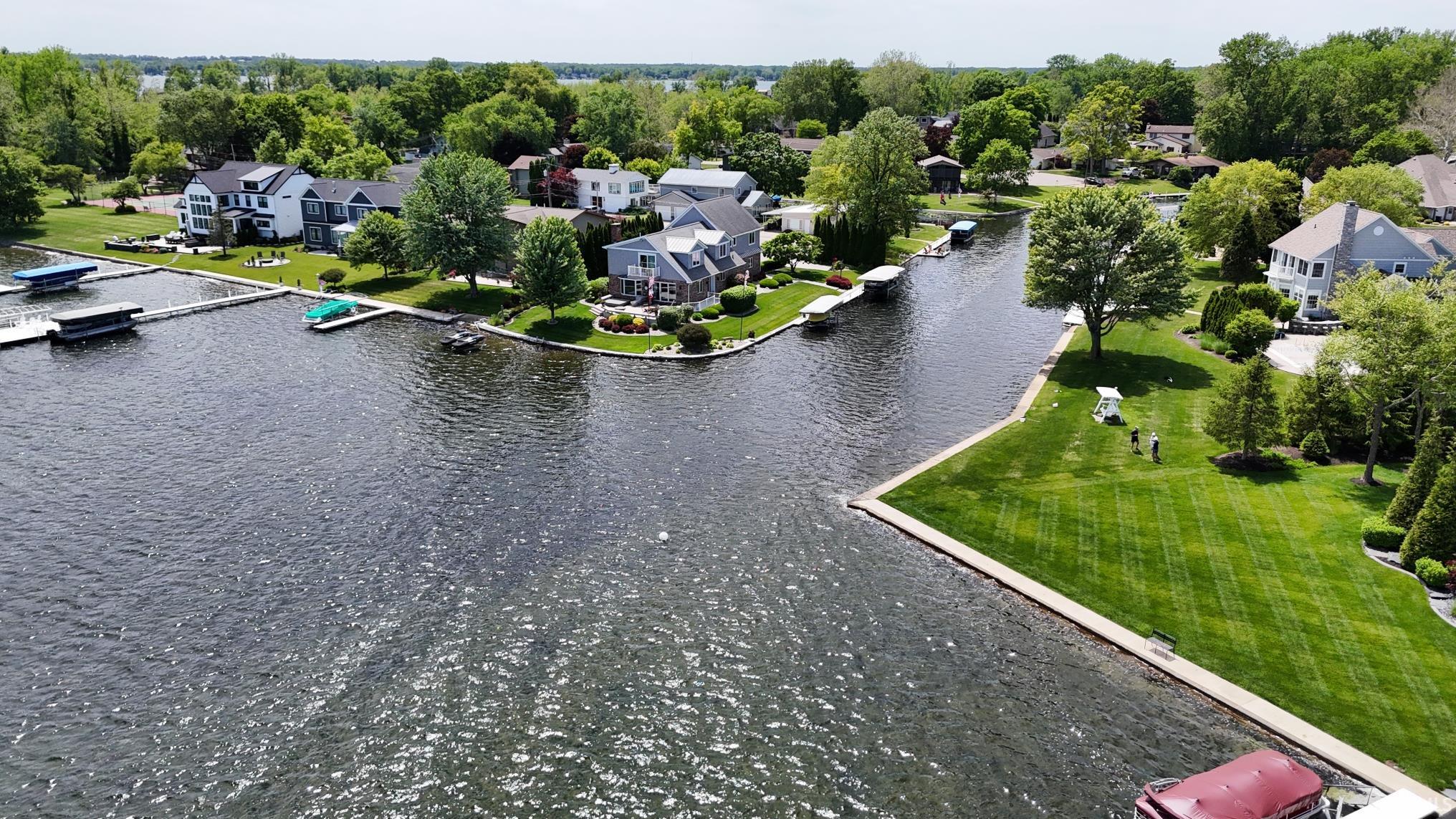 Waterfront property featuring a private boat dock, extensive green lawn, mature trees, and a concrete seawall
