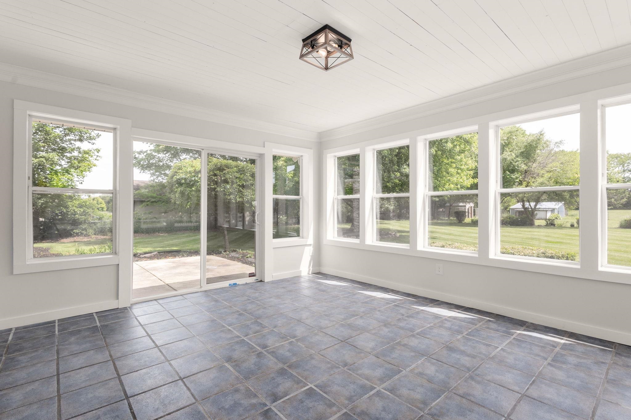 Sunroom with multiple windows, sliding glass door access to a patio, durable tile flooring, white planked ceiling, and a flush-mount ceiling light fixture