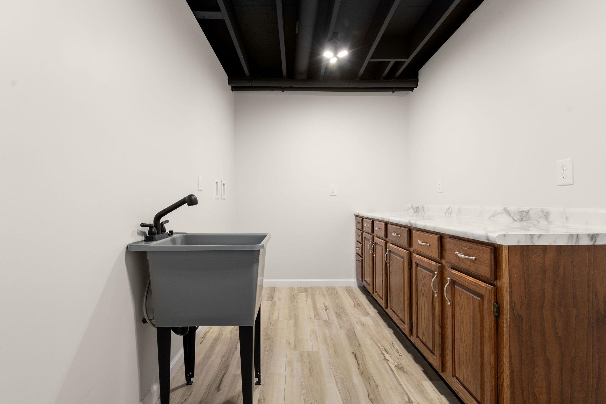 Utility room featuring a laundry sink with a matte black faucet, wood-finish flooring, white walls, and track lighting