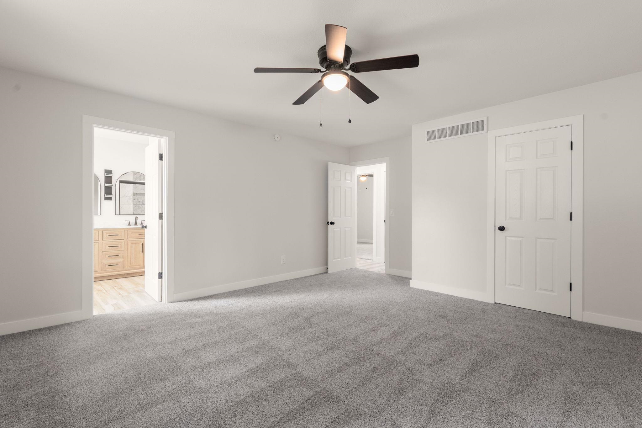 Spacious room featuring light gray walls, gray patterned carpet, a ceiling fan with integrated lighting, and white trim throughout