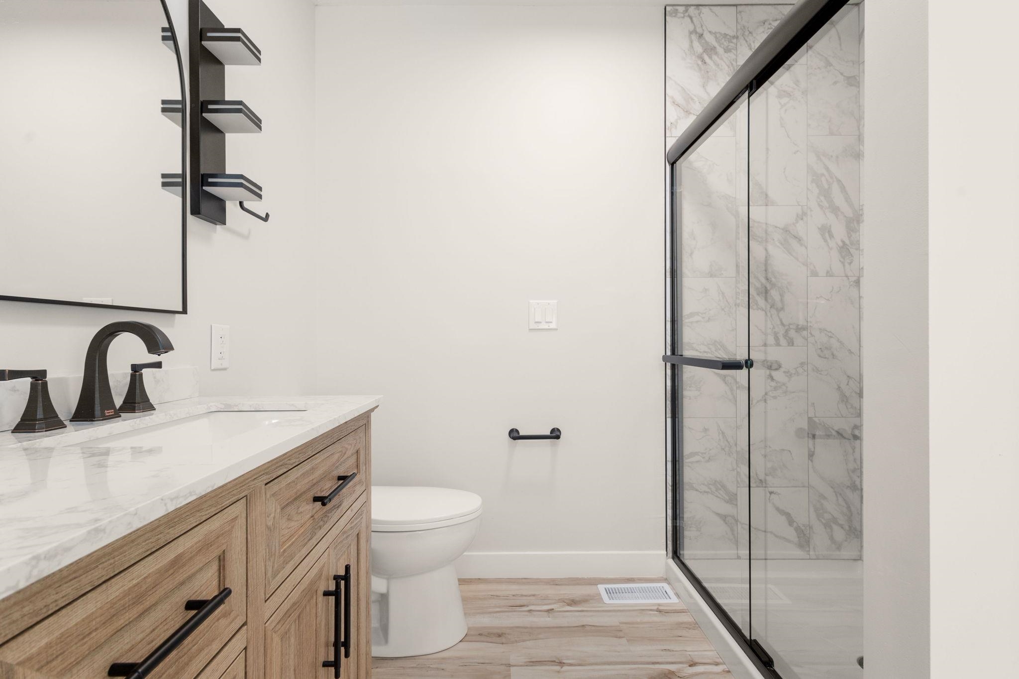 Contemporary bathroom featuring a spacious glass-enclosed shower with tile surround, a wood-finish vanity with a white countertop, and matte black hardware