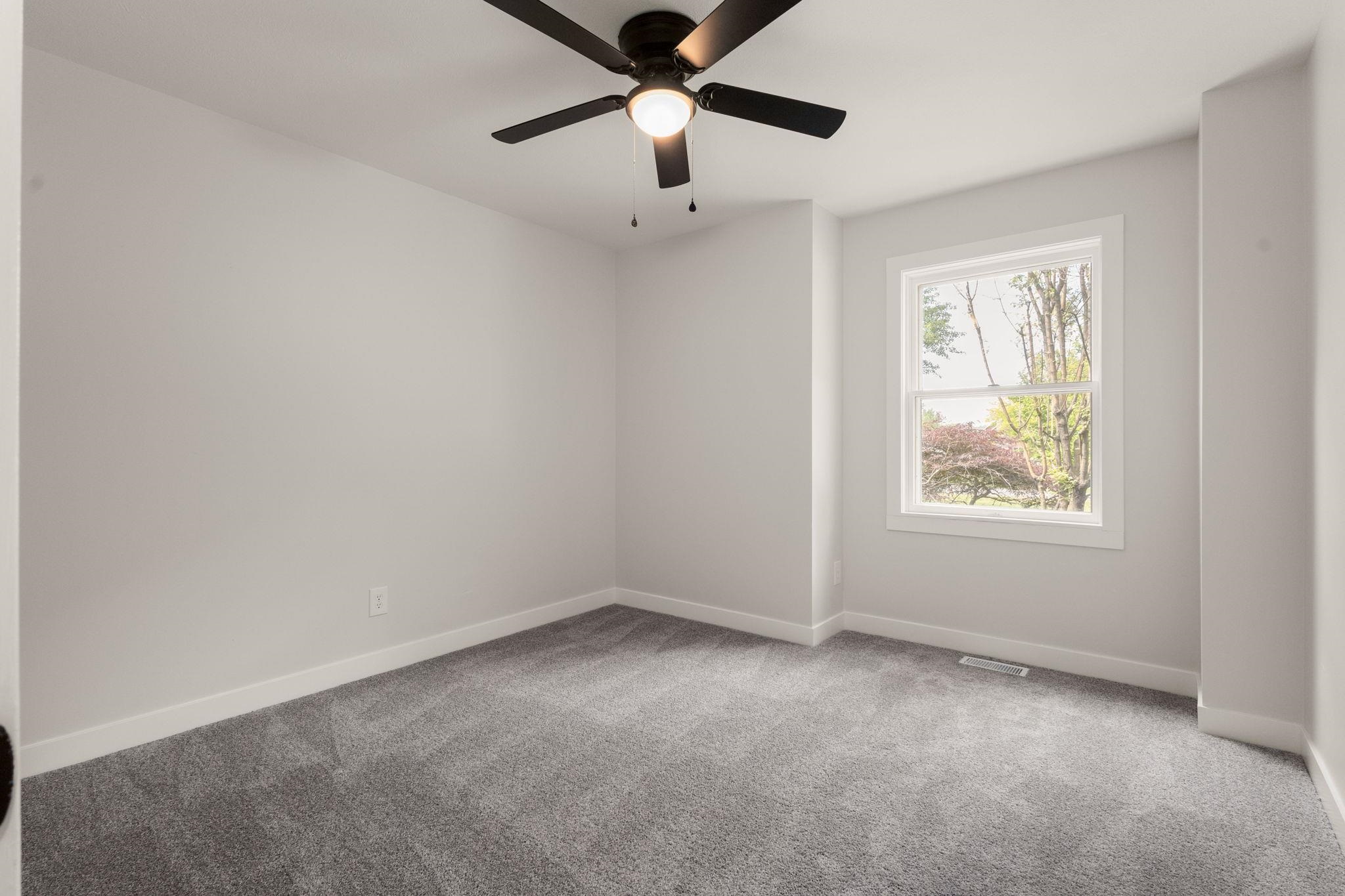 Neutral-toned room featuring a single window, a ceiling fan with integrated lighting, and gray carpet flooring