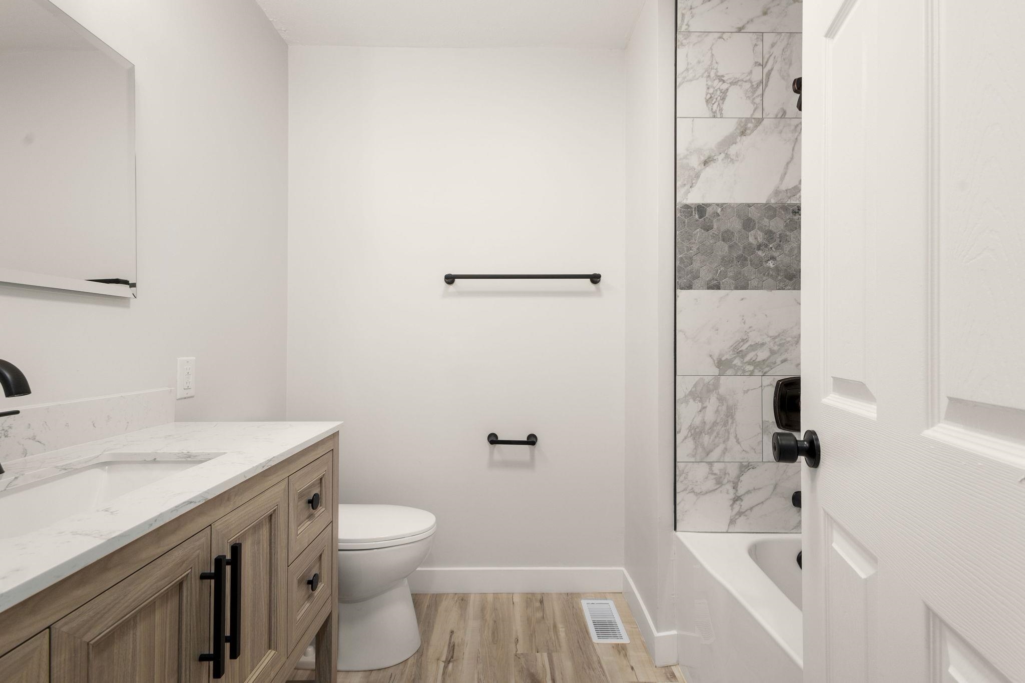 Bathroom featuring a wood-finish vanity with a quartz countertop, an undermount sink, and matte black hardware