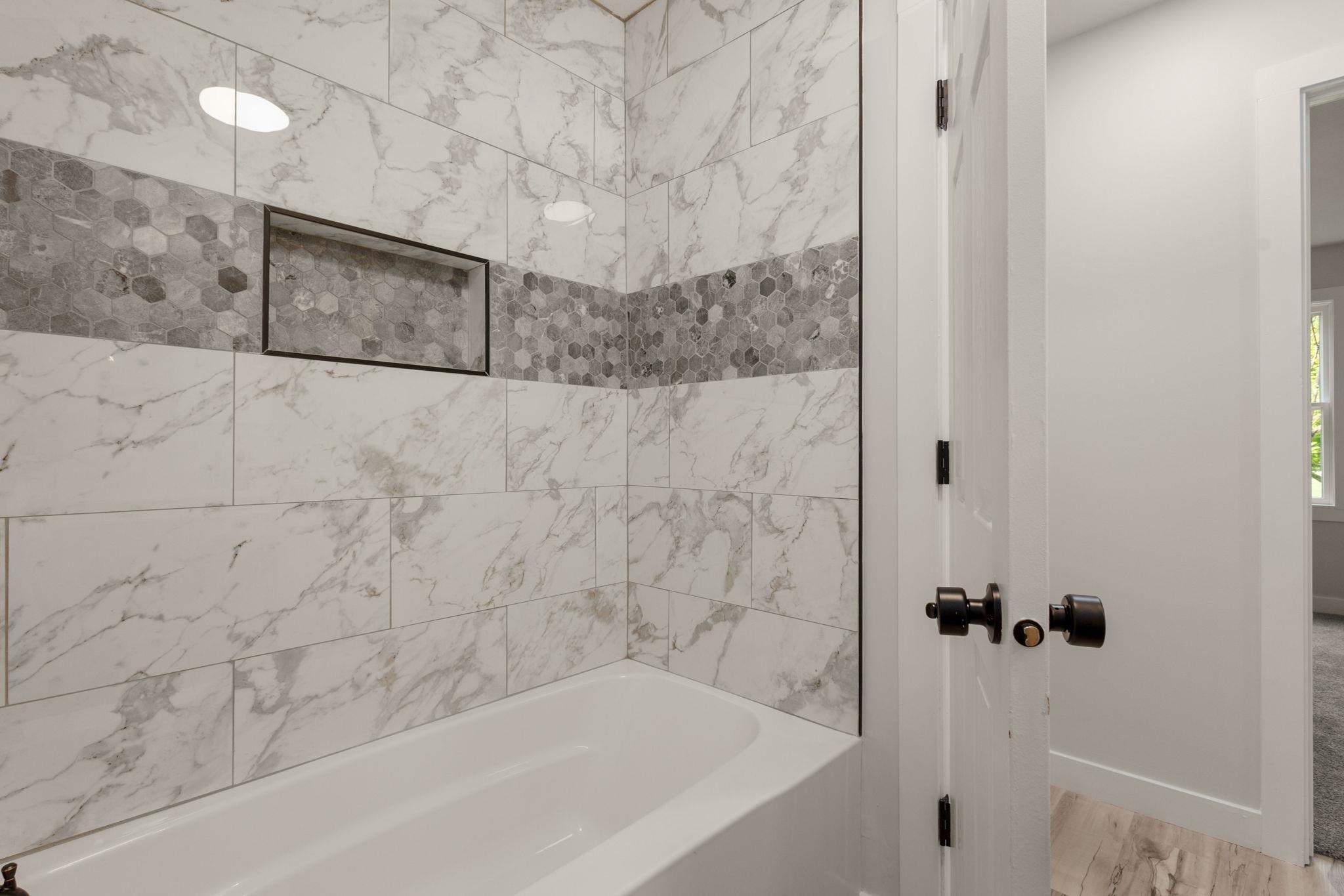 Tub-shower combination featuring white subway tile with gray veining, a decorative band of hexagonal mosaic tile, and a built-in shower niche