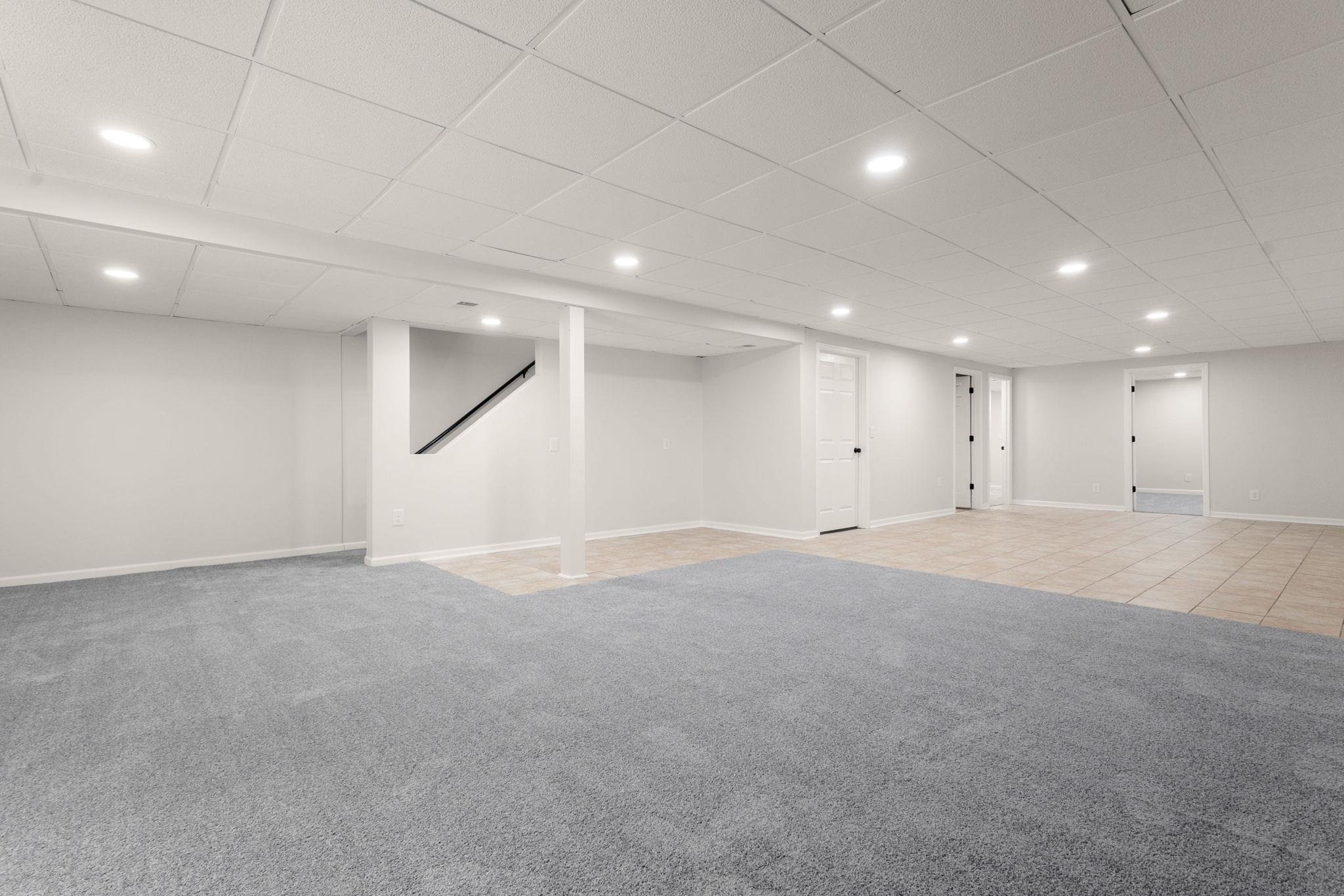 Spacious lower level featuring recessed lighting, a drop ceiling, and a combination of gray carpeting and neutral-toned tile flooring