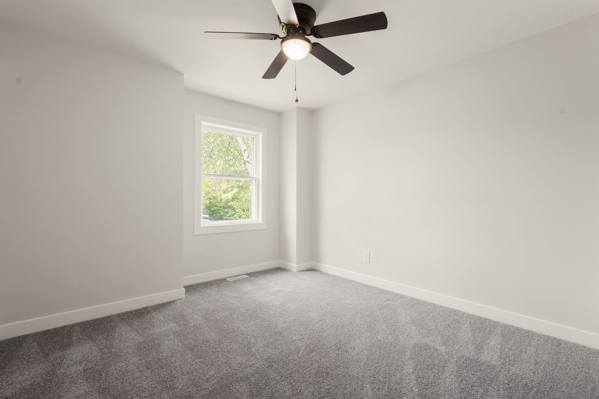 Bright room featuring a window with white trim, gray carpeting, white walls, and a ceiling fan with light fixture