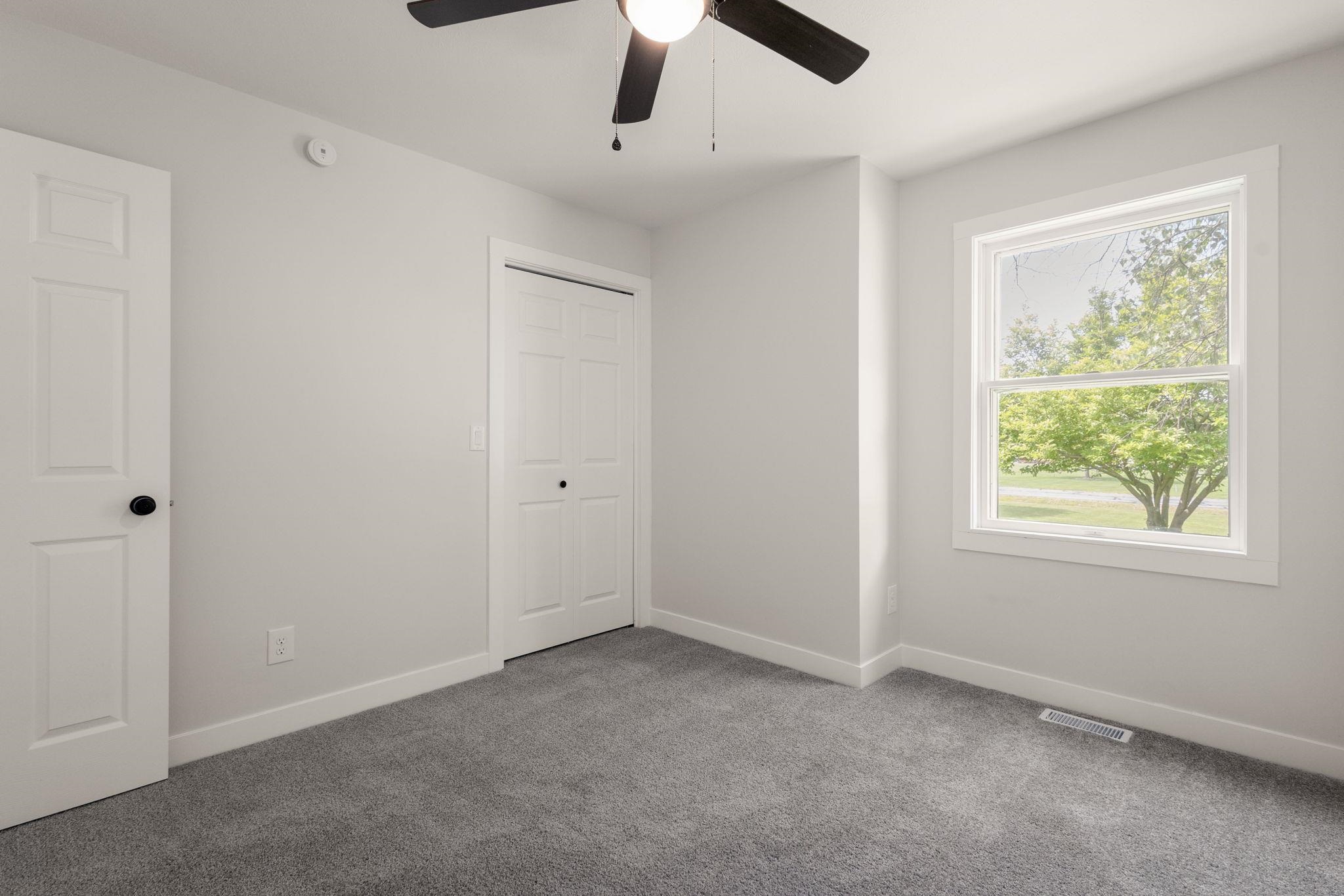 Bright room featuring a ceiling fan with integrated lighting, a single window, a bi-fold closet door, a paneled entry door, and gray carpeting