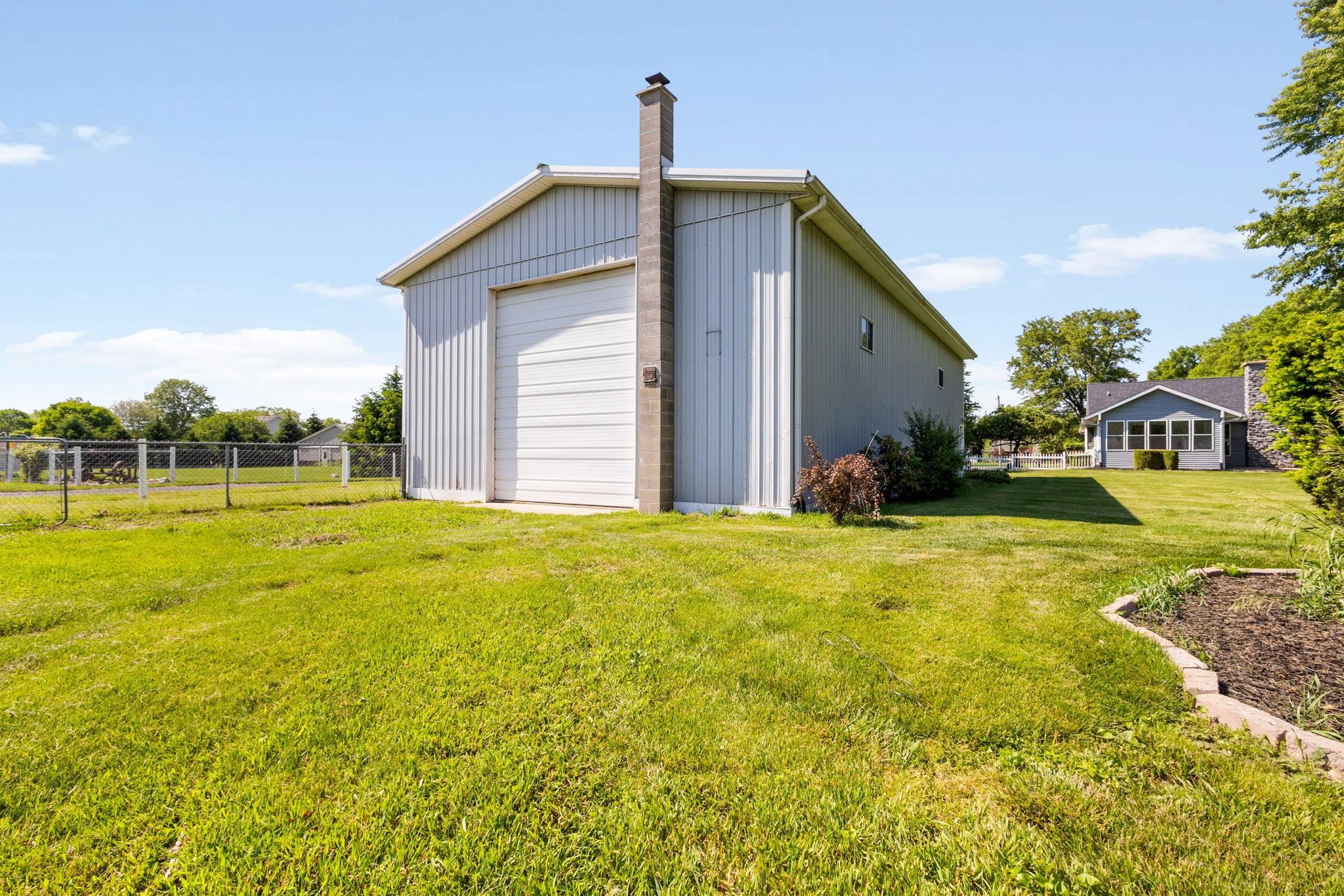 Large metal outbuilding featuring a white roll-up garage door, a brick chimney, and corrugated siding