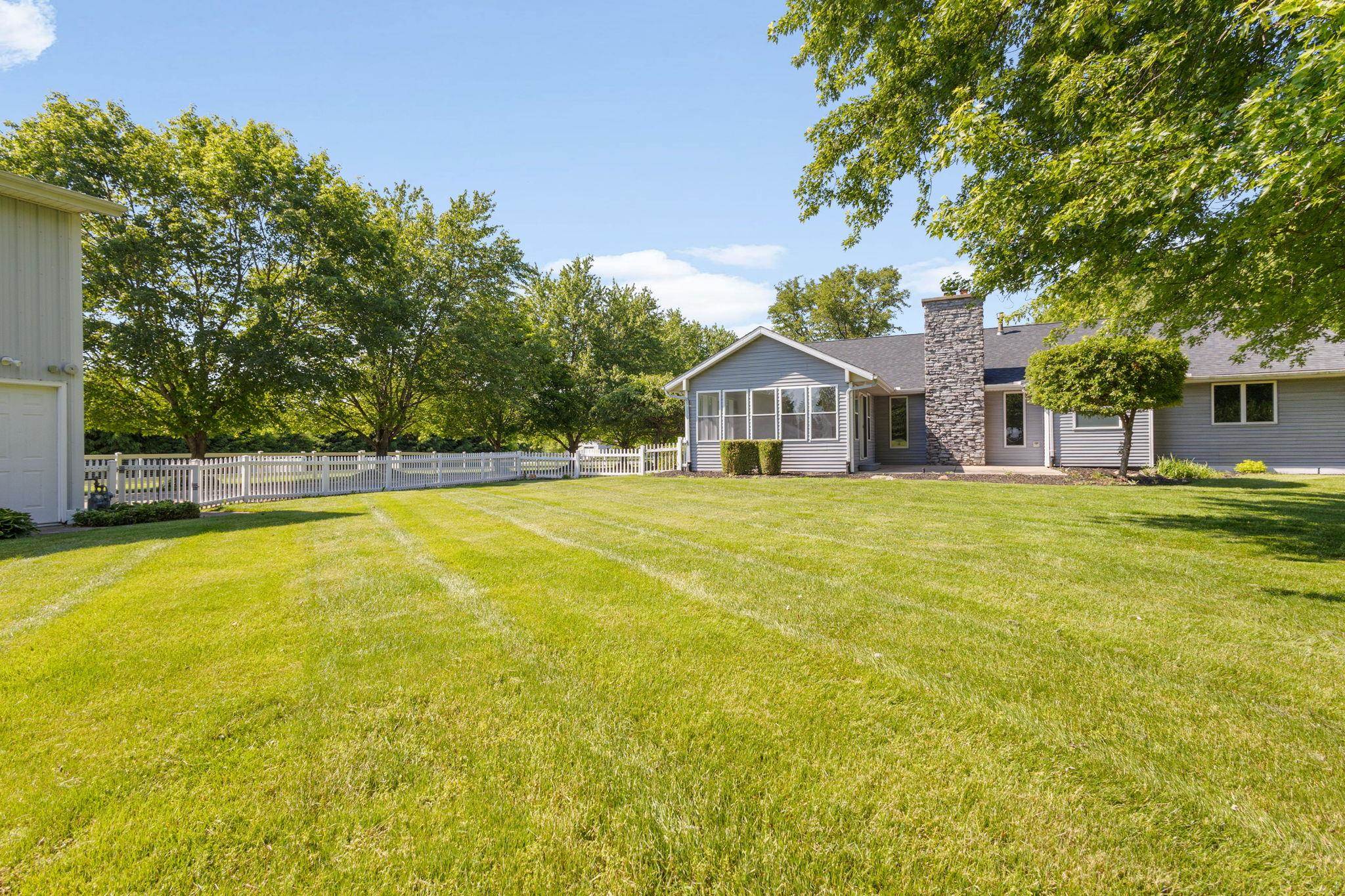 Expansive green lawn framed by mature trees and a white picket fence
