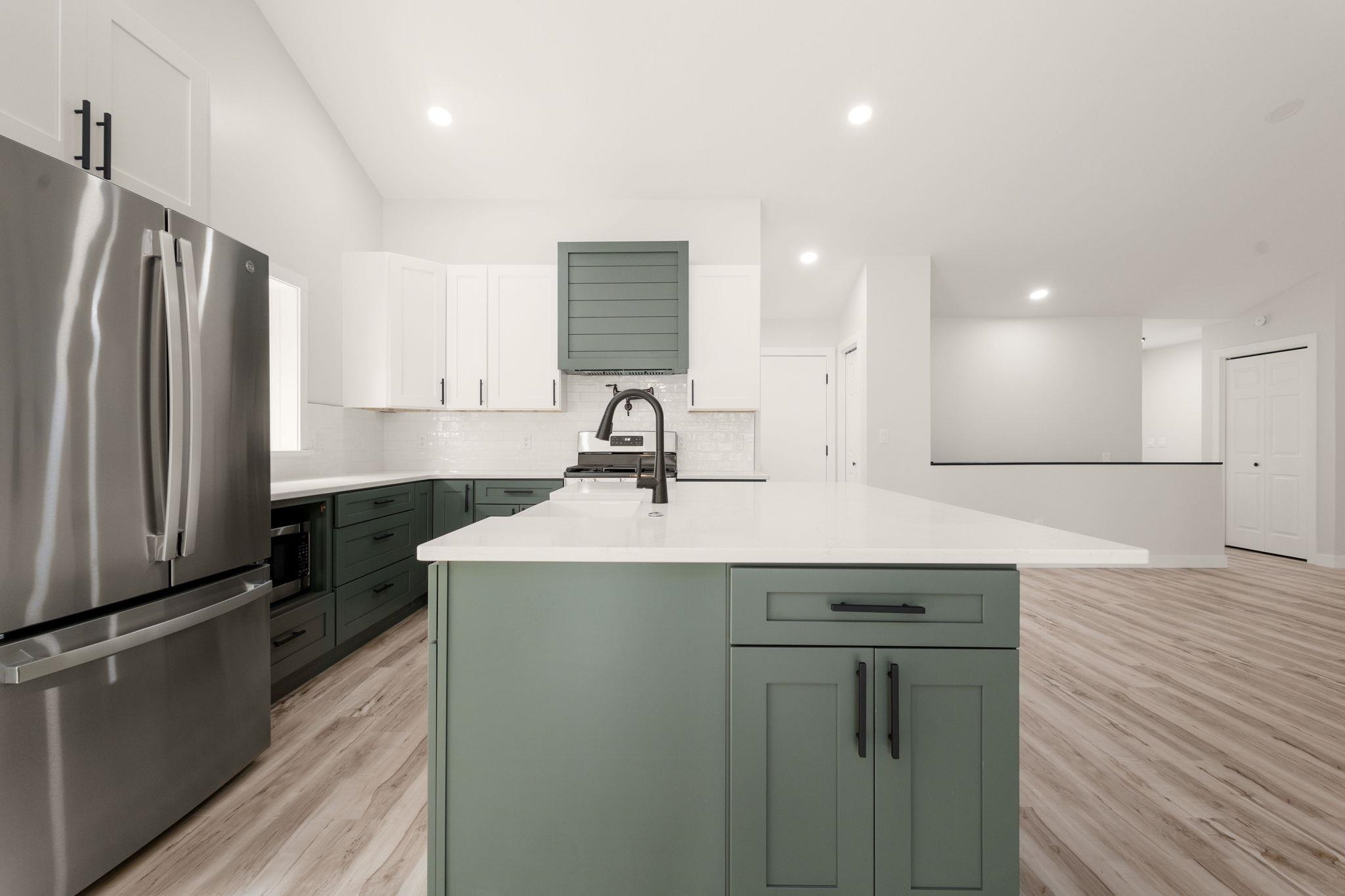 Modern kitchen featuring a large central island, stainless steel appliances, two-tone cabinetry with matte black hardware, white subway tile backsplash, and wood-finish flooring