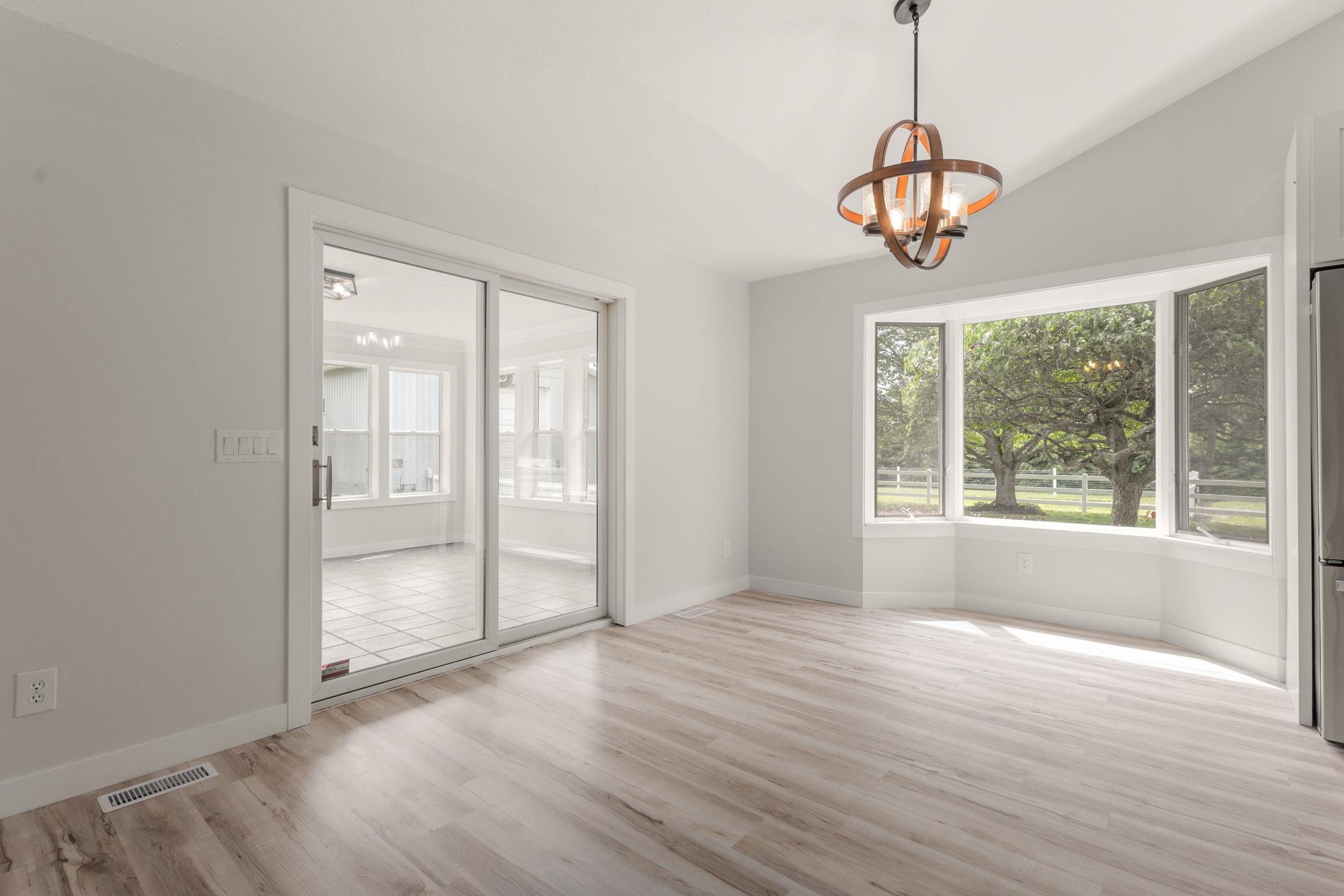 Spacious area featuring light wood-finish flooring, a contemporary chandelier, a large bay window, and a sliding glass door