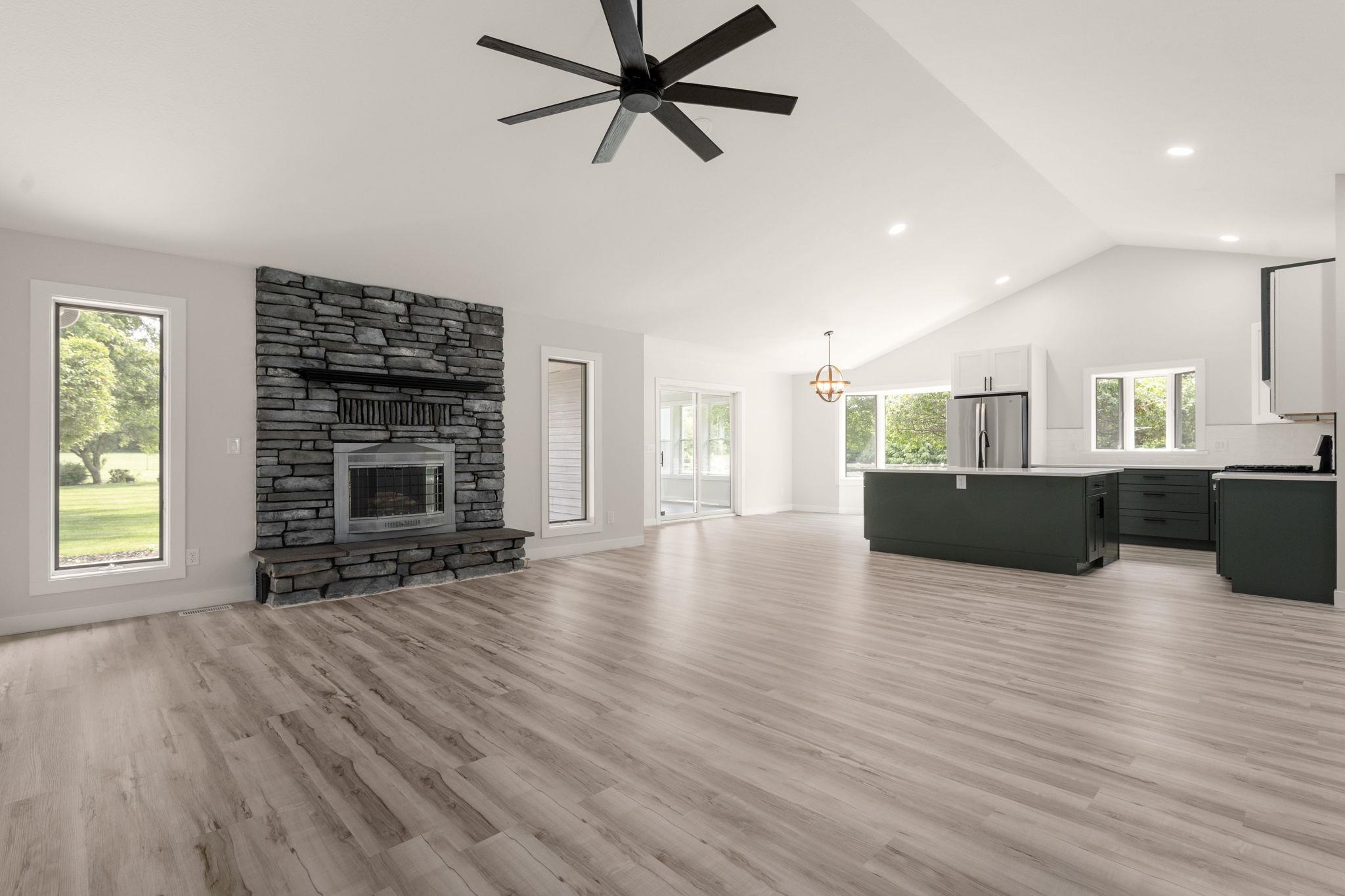 Open concept living area featuring wood-finish flooring, a stone-clad fireplace, vaulted ceilings, a contemporary ceiling fan, and recessed lighting