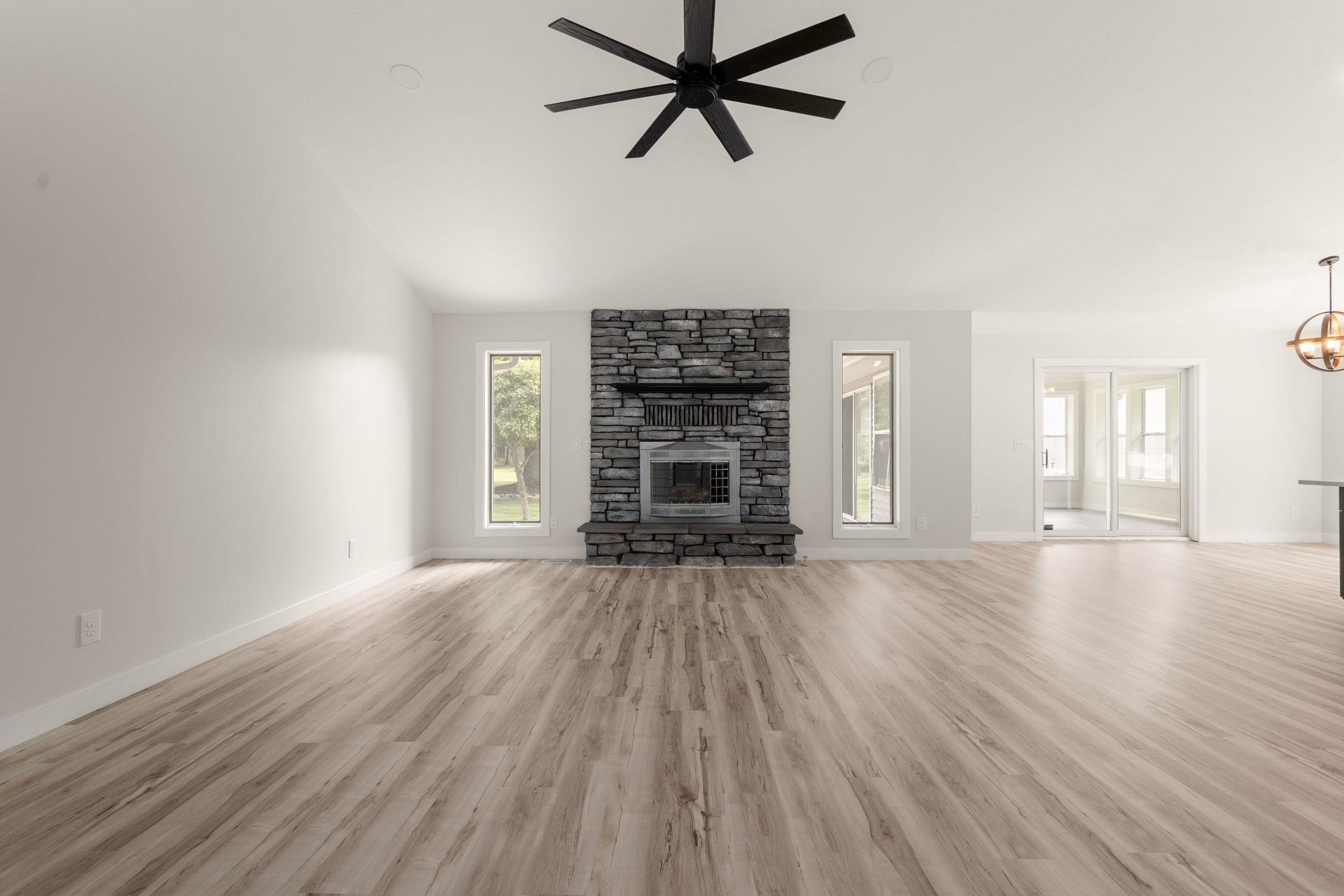 Spacious living area featuring a stone fireplace with a raised hearth, wood-finish flooring, and a contemporary ceiling fan