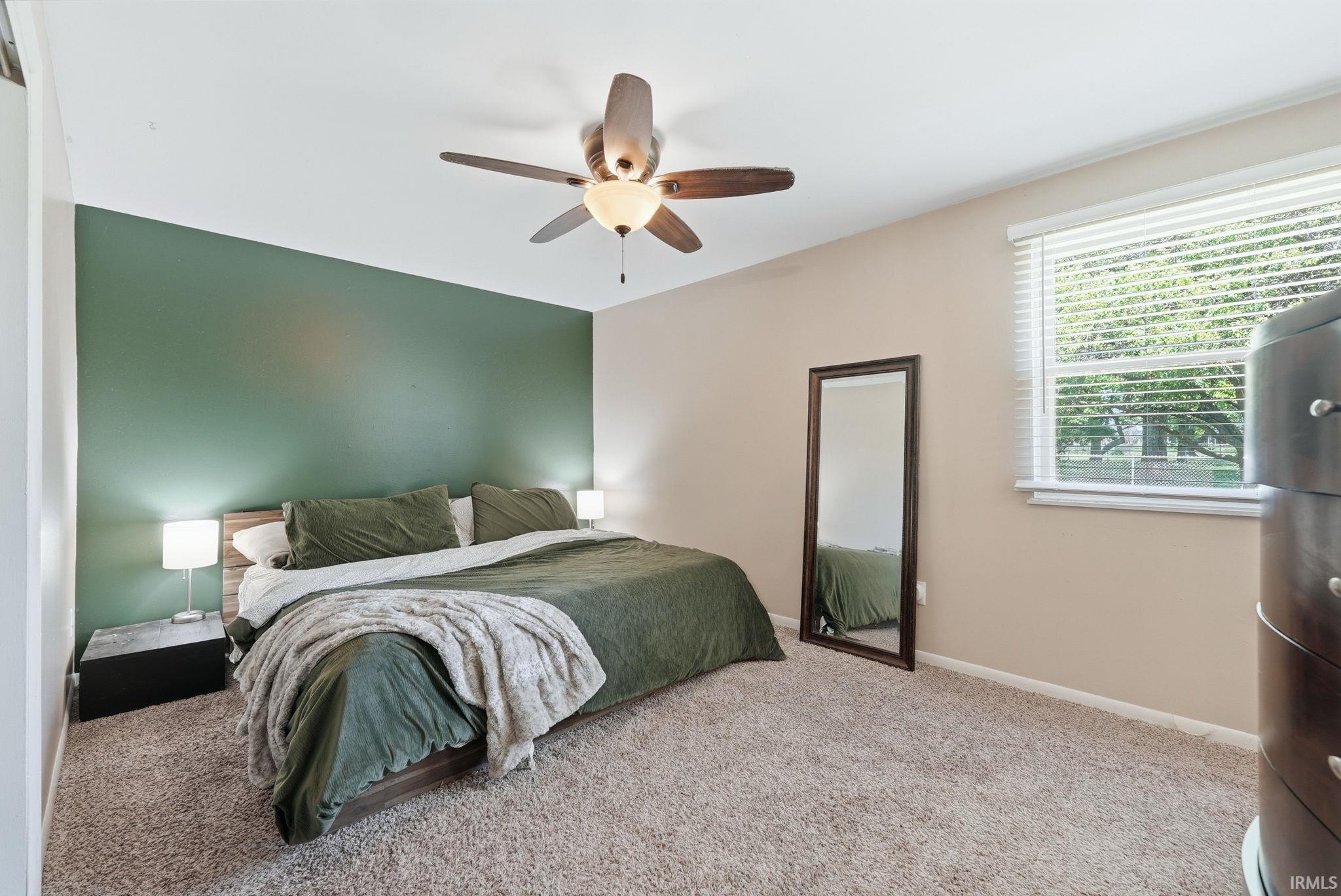 Carpeted room featuring a single window with blinds, a ceiling fan with light, and a green accent wall