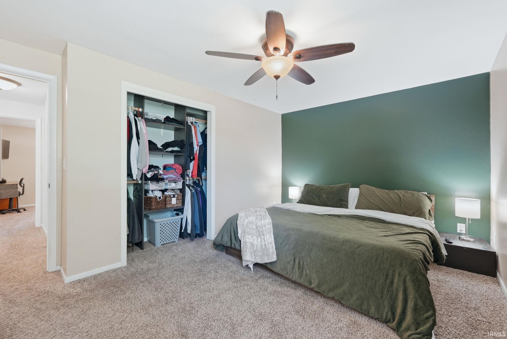 Carpeted bedroom featuring a ceiling fan with integrated lighting, a contrasting accent wall, and a built-in closet with sliding doors and shelving
